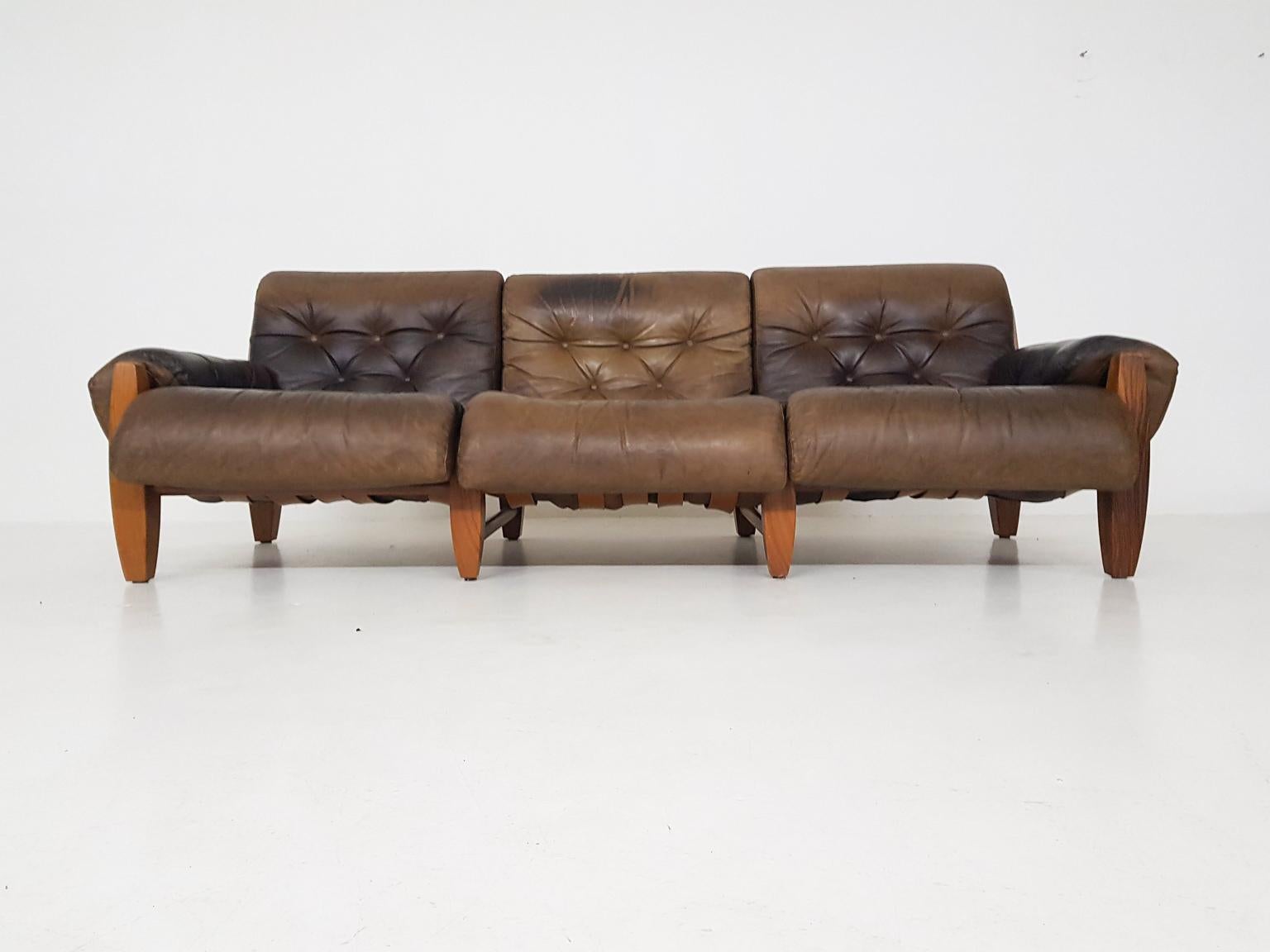 Oak frame and brown leather three-seat sofa attributed to Sergio Rodrigues, Jean Gillon or Percival Lafer.

We haven't found its designer yet, but we think it has Brazilian roots. The wooden frame, leather straps and the large hanging leather