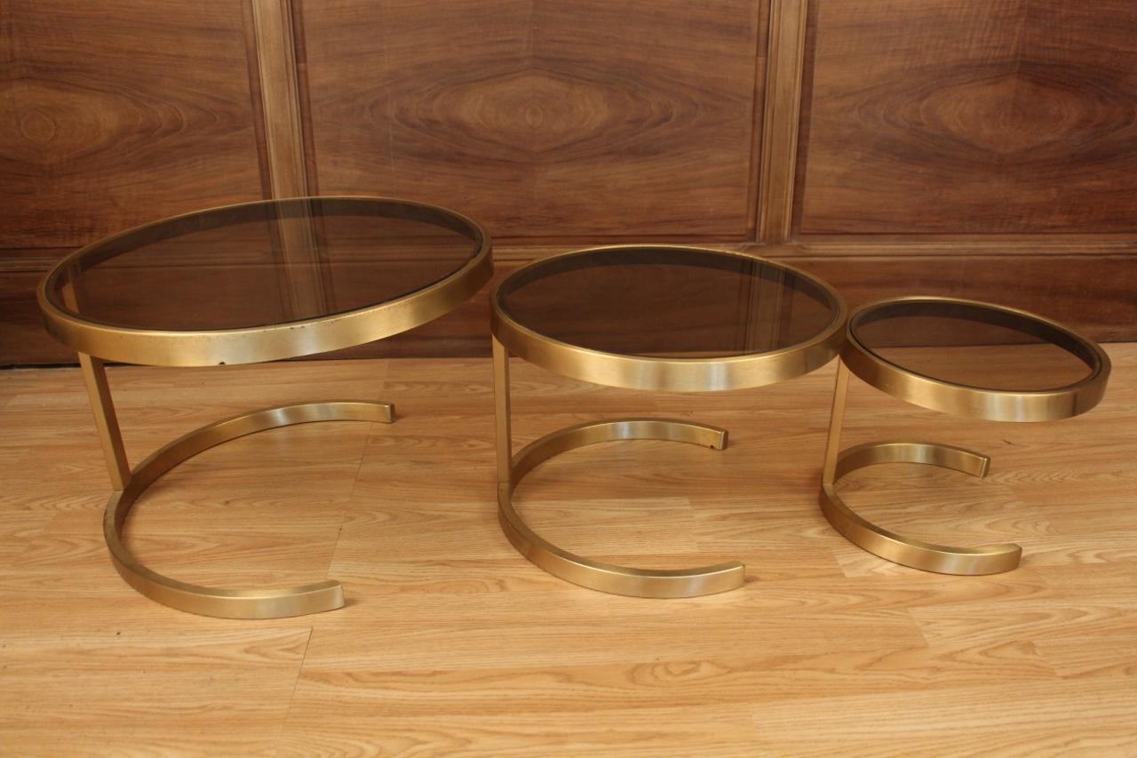 set of three nesting tables from the 70s, in very good condition, smoked glass tops, gilt metal legs large table: 34 cm high by 52 cm in diameter medium table: 29 cm high by 42 cm in diameter small table: 24 cm high by 32 cm in diameter.