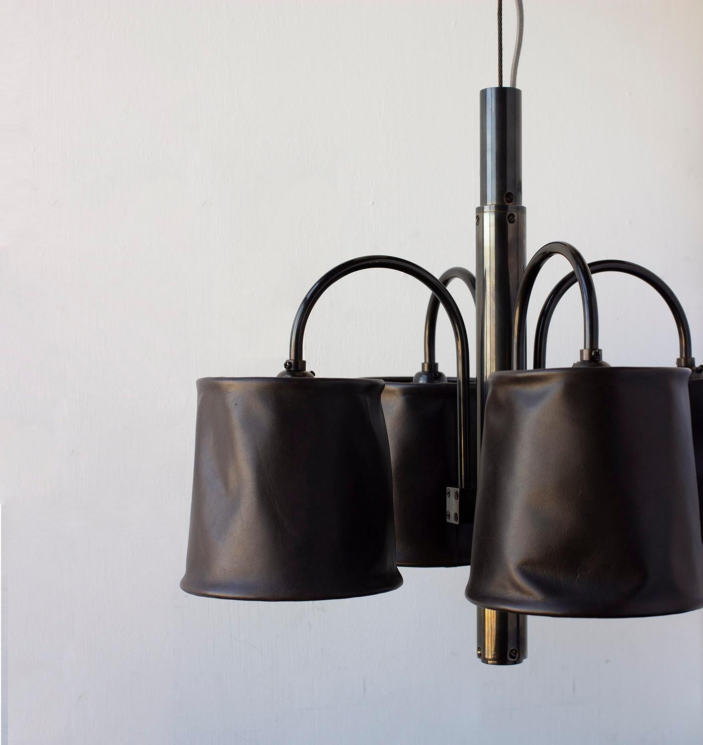 Solid machined brass, soft hand-dyed waxed leather shades, patinated copper tension wire with fabric cord. The opaque nature of leather creates an overall effect of directed ambient lighting well suited for over tables and dining areas. Hanging