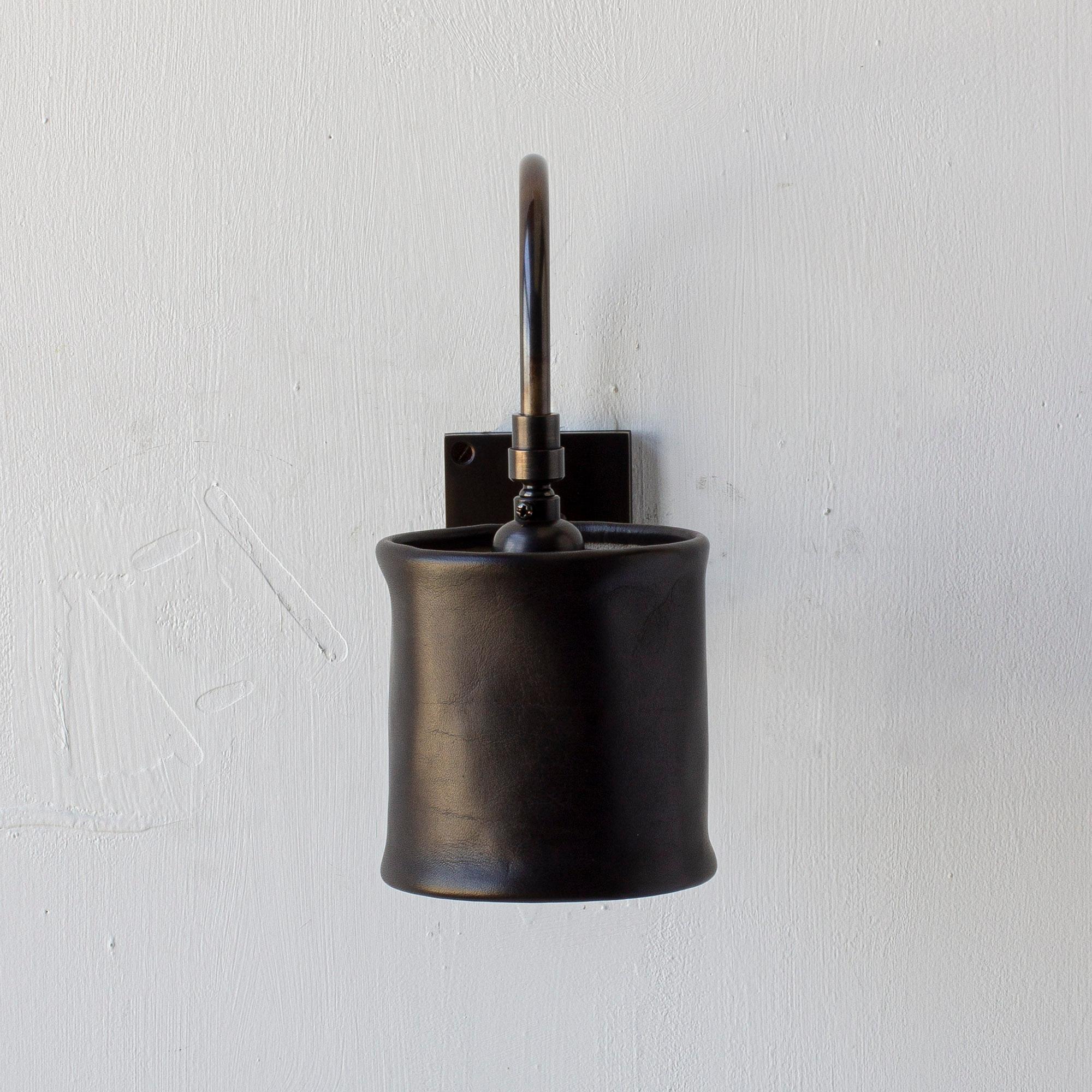 Solid machined brass in dark patinated finish, hand-dyed soft unstructured leather pivoting shade. All material finishes are living finishes: they will change and patina for the better with time and use. Backplate is made to fit only a single gang