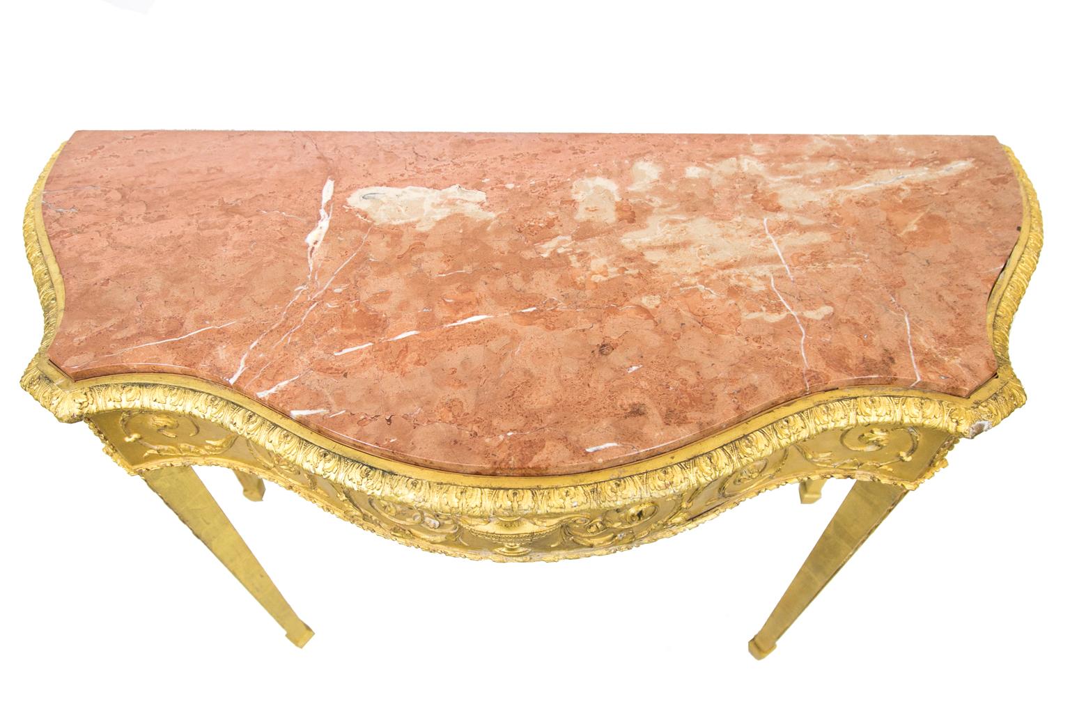 Serpentine English marble-top gilt console table, has applied acanthus molding, while the apron has applied floral arabesques. The legs, which terminate in spade feet, have applied bellflower. The marble is a 20th century replacement.
 