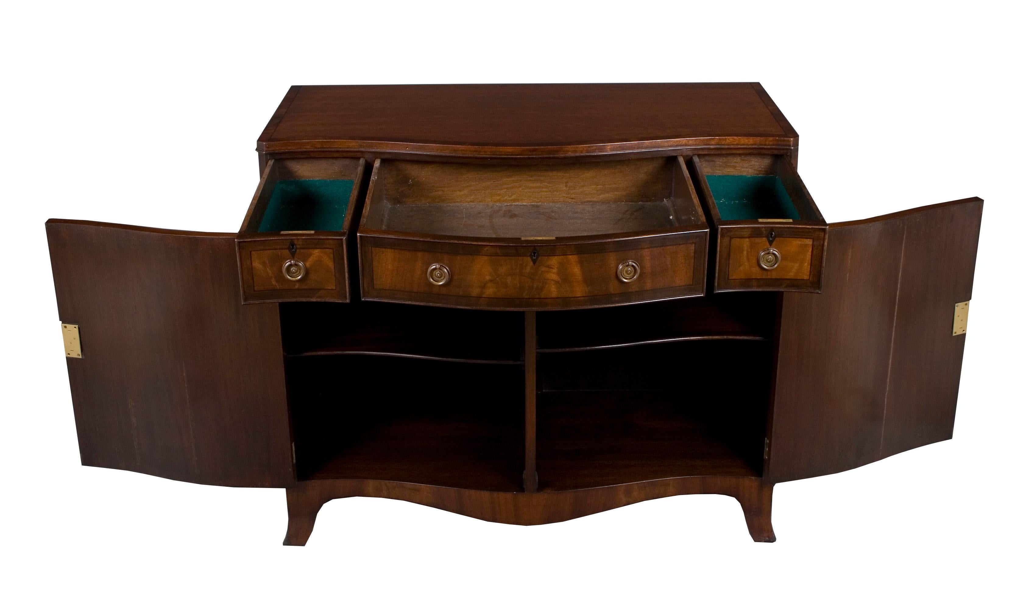 This unique buffet cabinet was made in England around the year 1960 of mahogany. The stunning serpentine front and black line ebony inlay come together to form a beautiful piece of furniture. A mahogany cross band on the top further and ebony inlaid