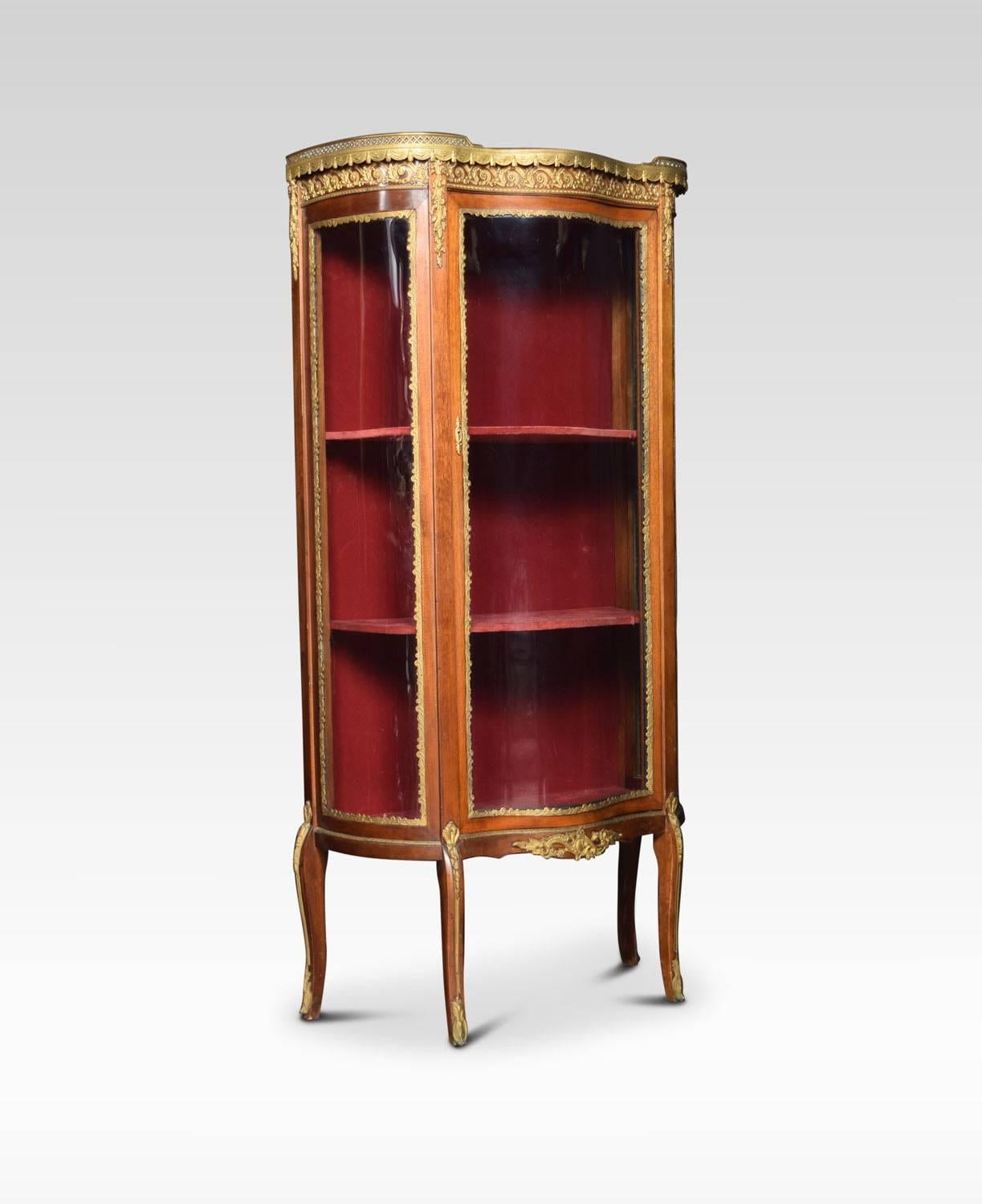 Mahogany display cabinet, the shaped marble top with raised three quarter ormolu gallery, above glass sides and serpentine fronted door enclosing upholstered interior with two fixed shelves. All raised on elegant curved legs with ormolu