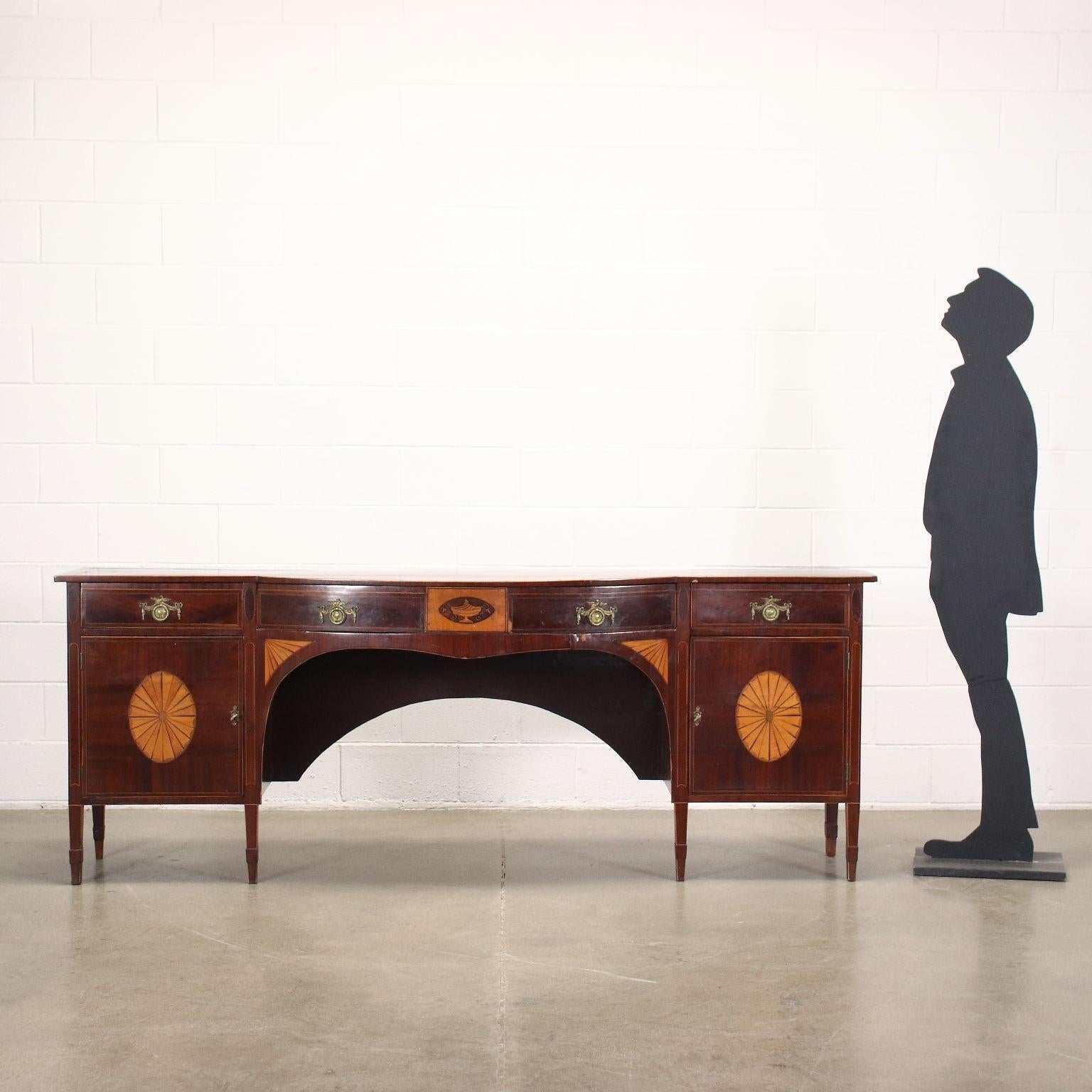 George III serpentine sideboard in mahogany veneer, England late 18th century. Top with maple threads, front with 3 drawers in the band, pair of doors and inlays in mahogany and maple including a vase and fan motifs on the doors. Lack of drawer