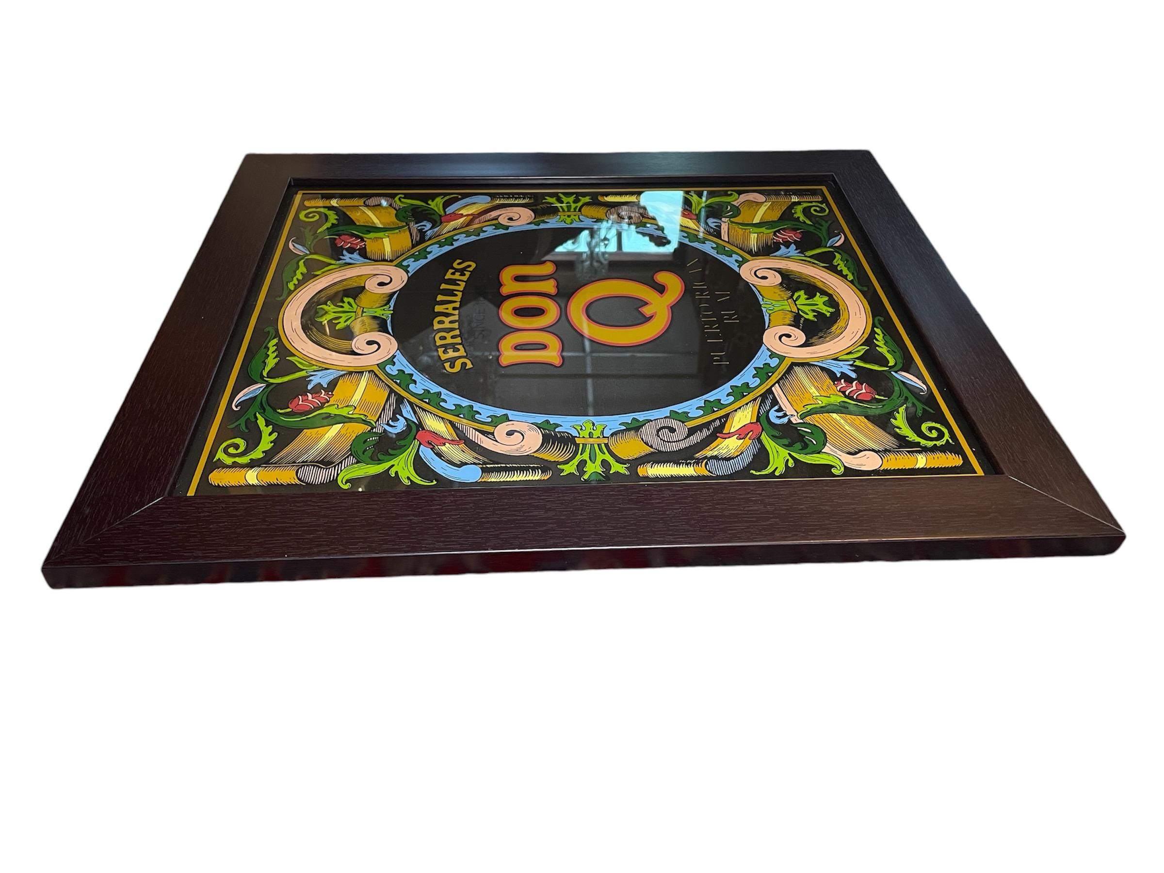This is a Serralles, Don Q Puerto Rican Rum Advertising Mirror Sign. It depicts  a rectangular mirror with a large oval shield like design with the big letters identifying the liquor in the center of it. A garland of trefoils and C-scrolls adorn the
