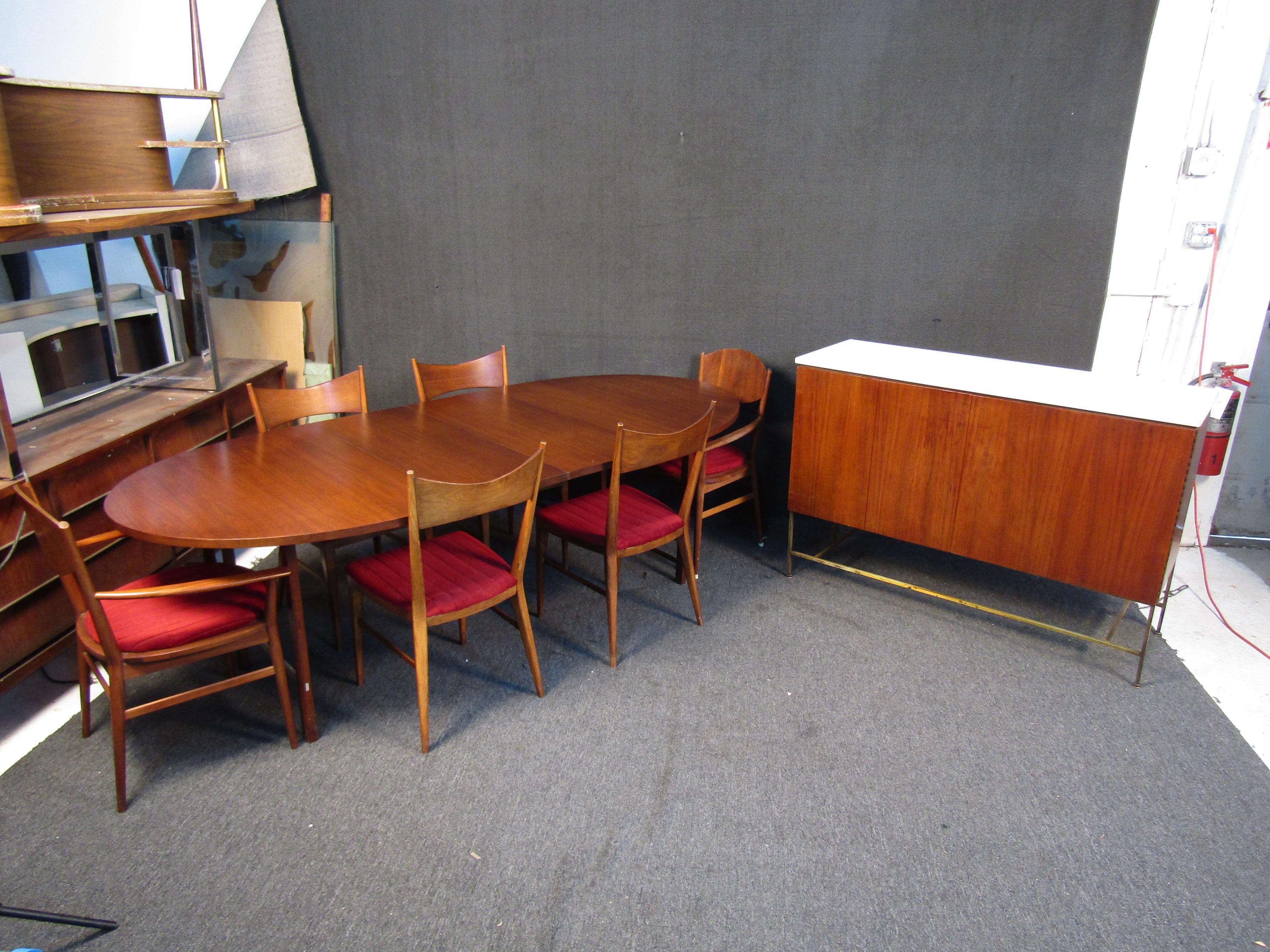 Add timeless Mid-Century Modern style to your dining room with this vintage set by Paul McCobb. It includes an expanding dining table, six chairs (2 with arms, 4 without), and a large server, all in rich walnut. Please confirm item location with