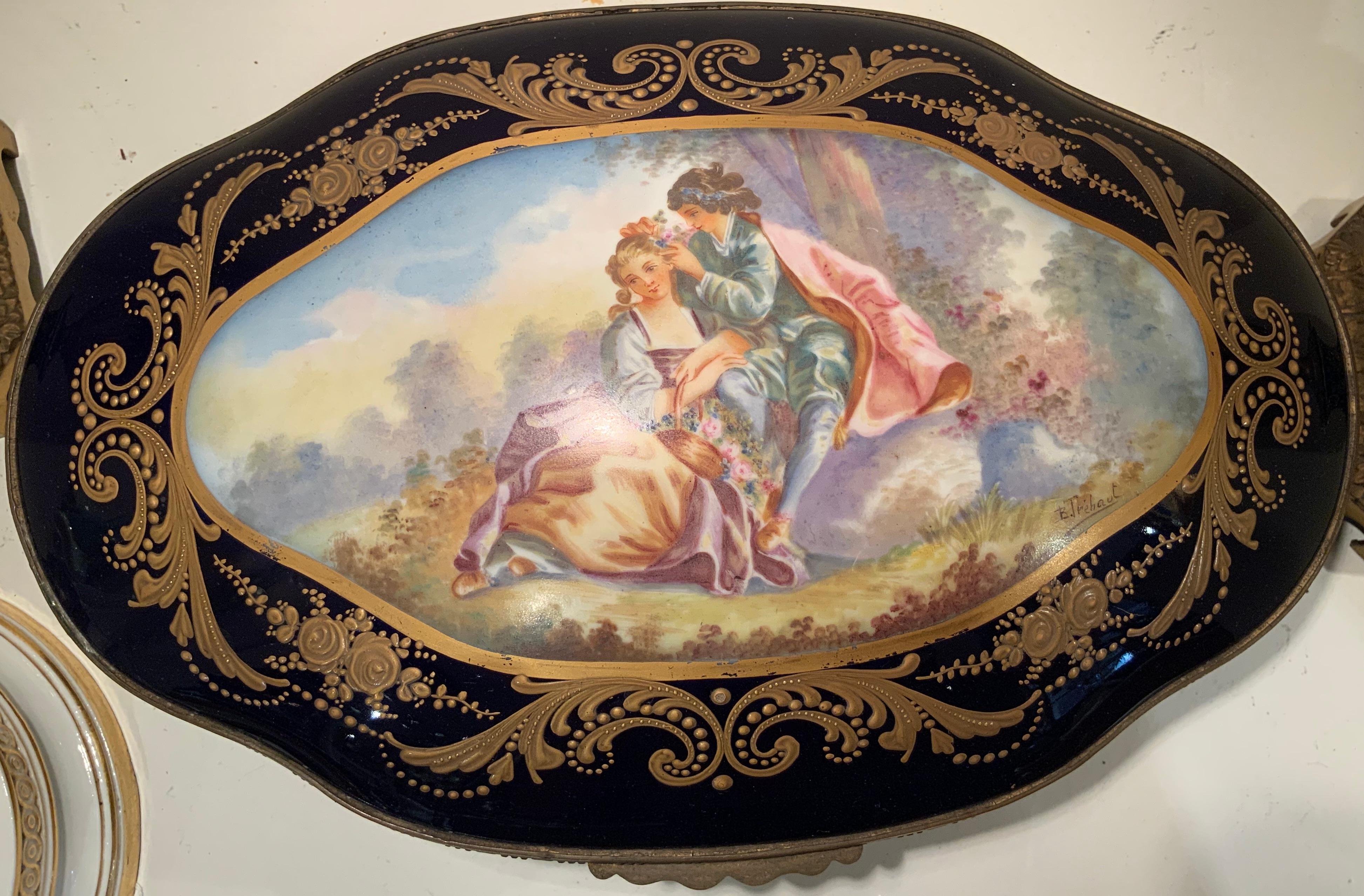 A background of dark cobalt blue with gilding details of scrolls and dots alternated with roses and foliage decorate this vanity box. The dome aspect of the lid features a hand painted romantic pastoral scene of a couple signed by B. Tre’haut. The