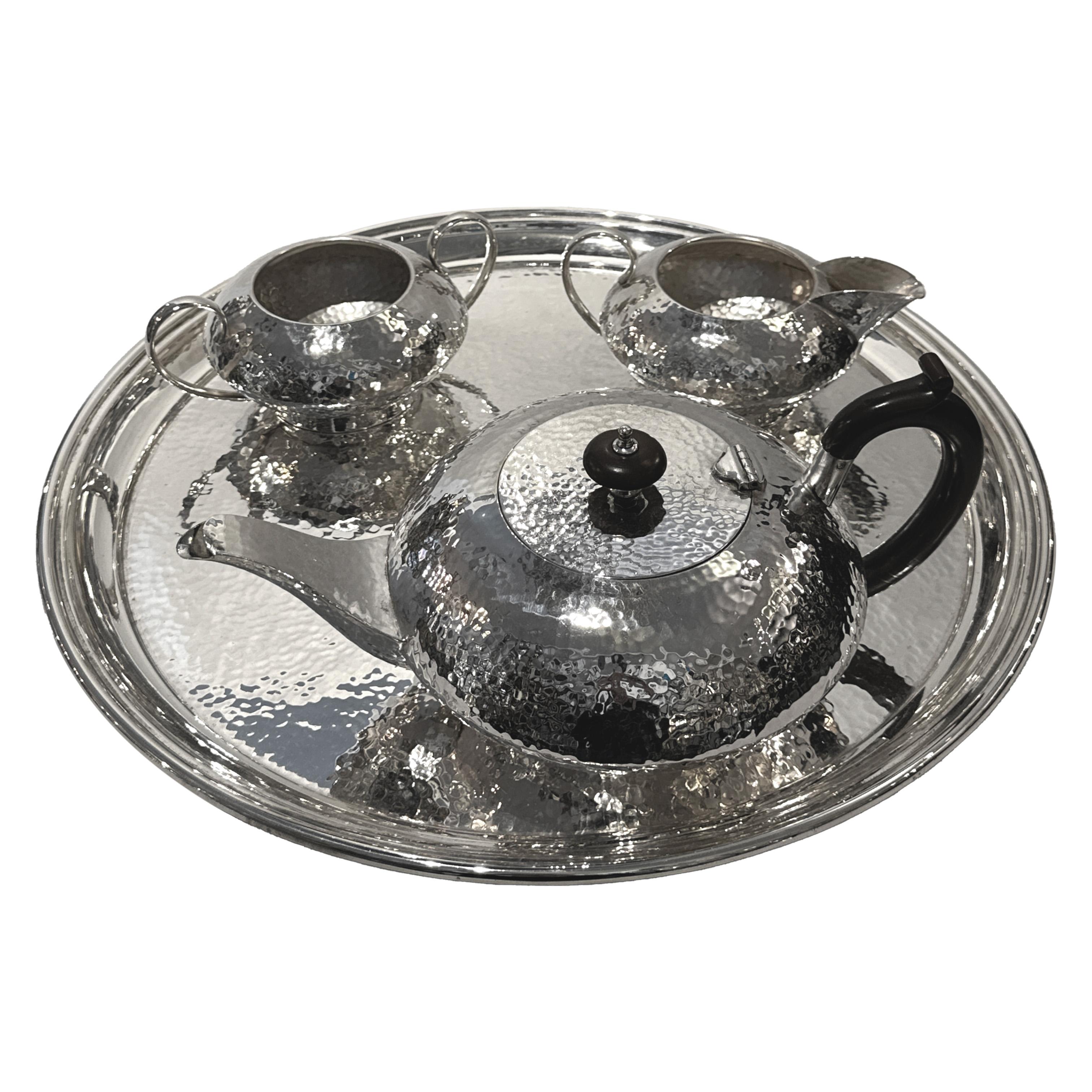 A striking and refined Art Deco four-piece tea service in hammered silverplate, comprising a teapot, milk jug, sugar bowl, and matching circular tray. This visually dynamic ensemble showcases the distinctive aesthetic of the late 19th century, with