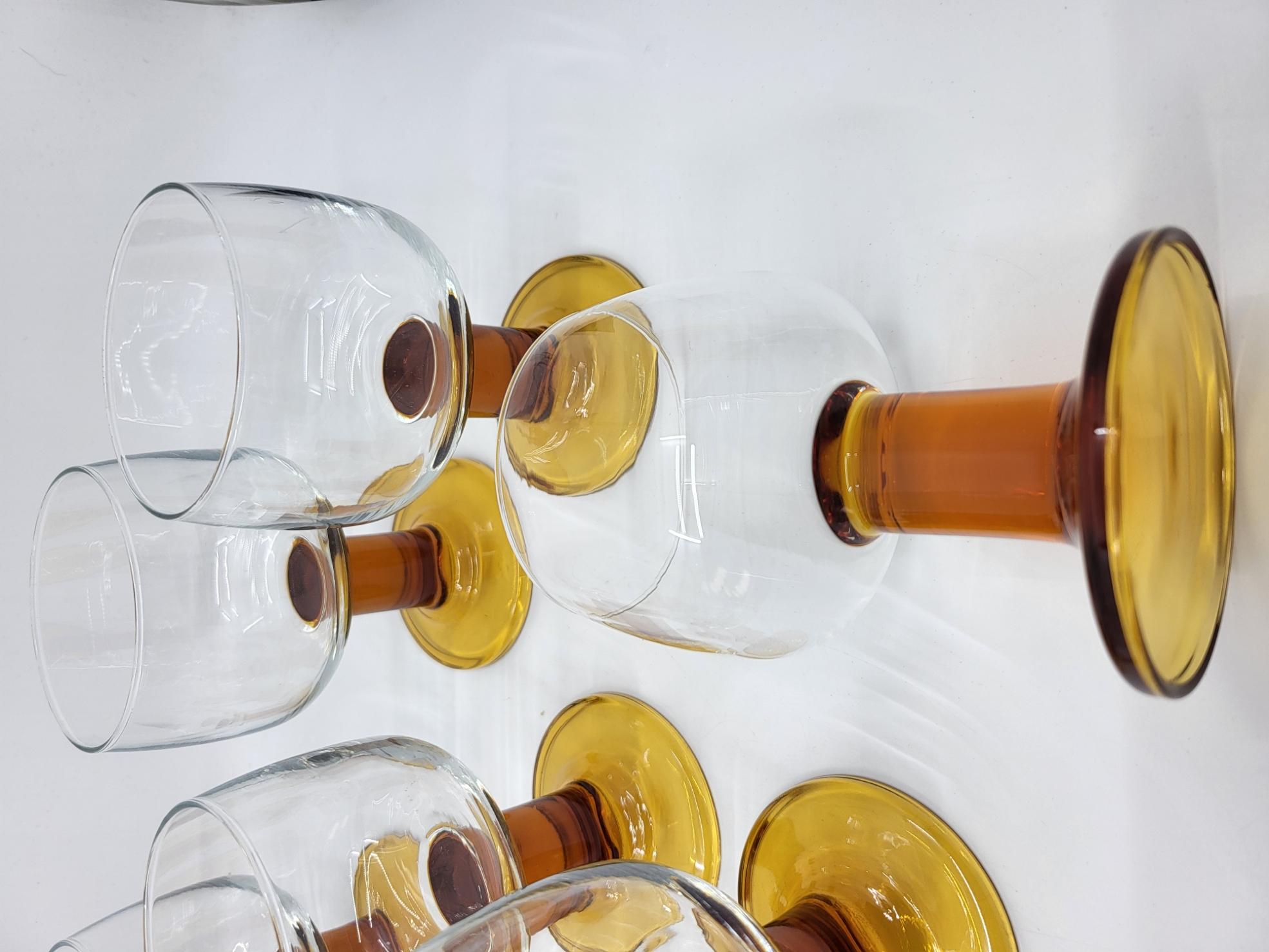 Sublimez vos tables avec cet ensemble unique de huit verres à pied vintage des années 1970 ! 
Chacun de ces verres arbore une élégante base en verre ambré, ajoutant une touche rétro et chaleureuse à votre service. Parfaits pour déguster des vins,