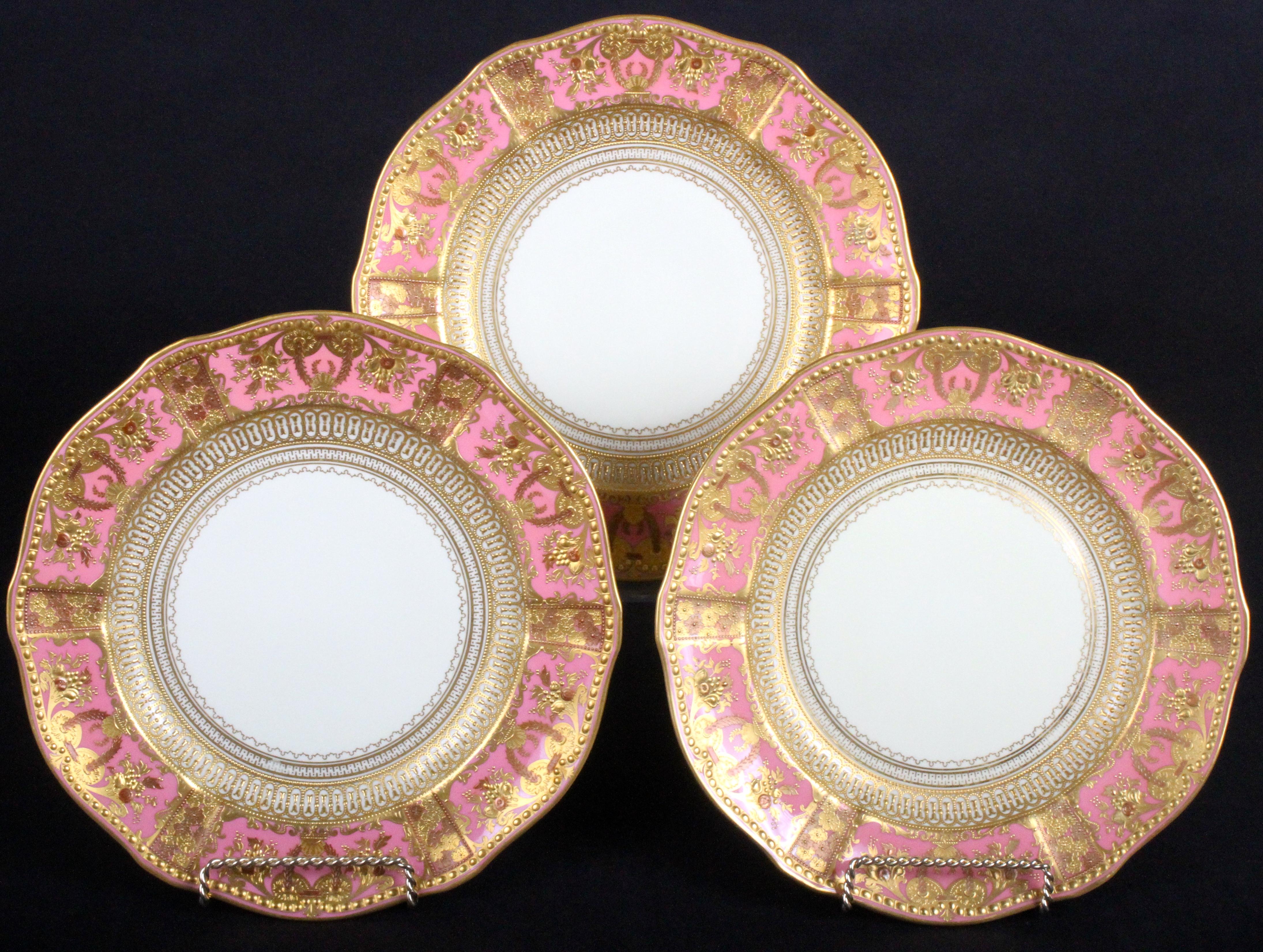 These 12 ornate service or dinner plates are from the esteemed Royal Crown Derby firm of Derby, England. The plate rim is divided into 6 panels that feature neoclassical motifs of cornucopia, flowers and laurel garland, the panels are separated by 6