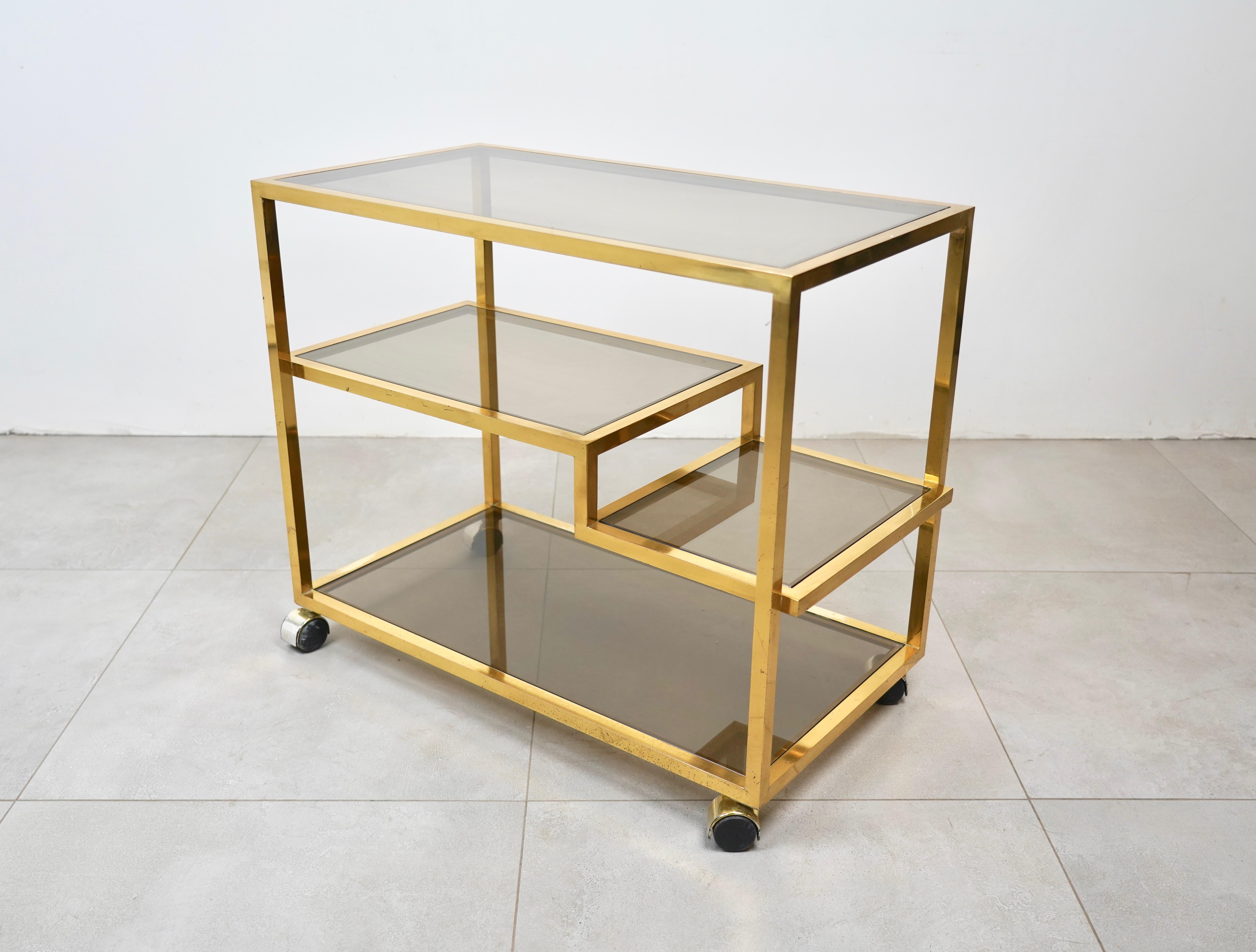 This vintage brass and smoked glass serving cart features unique midcentury design, combining simple lines and plenty of room for storage or service. In the style of to the Italian designer Romeo Rega. Made in Italy in the 1970s.
