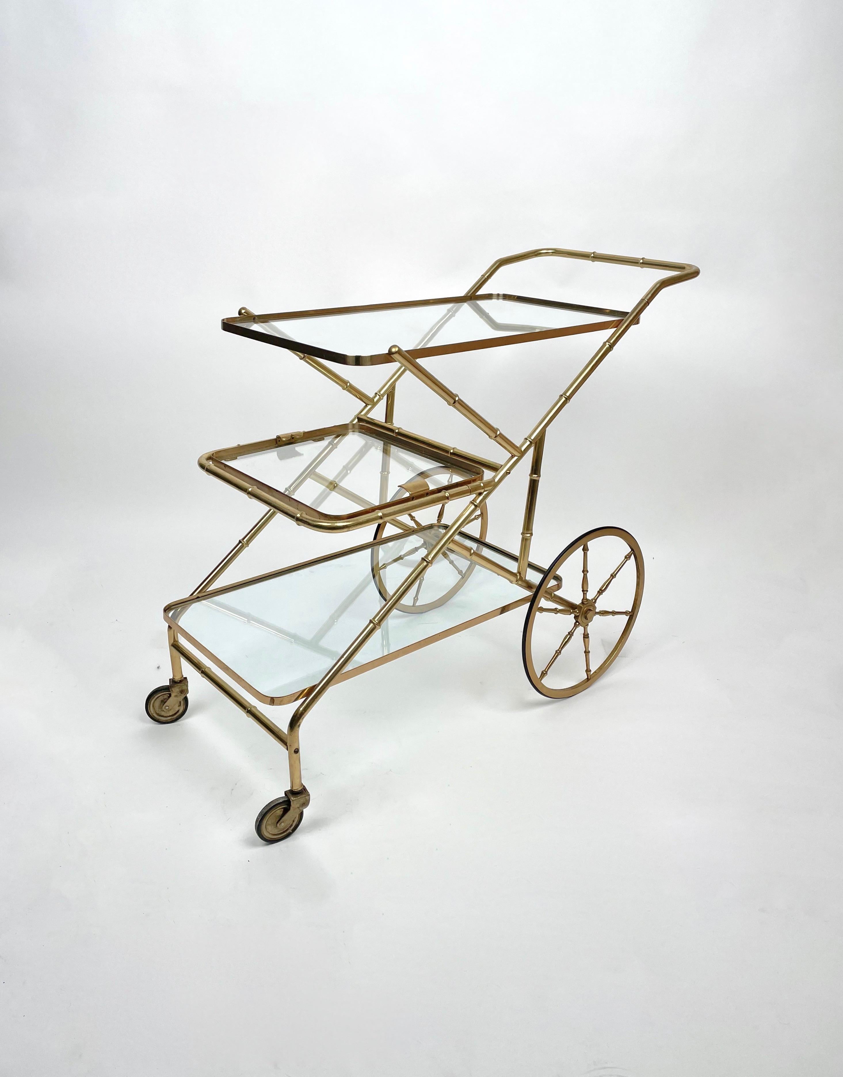 Serving bar cart in a brass, faux bamboo structure with three glass shelves, the middle one being removable, on wheels.

Made in Italy in the 1960s.