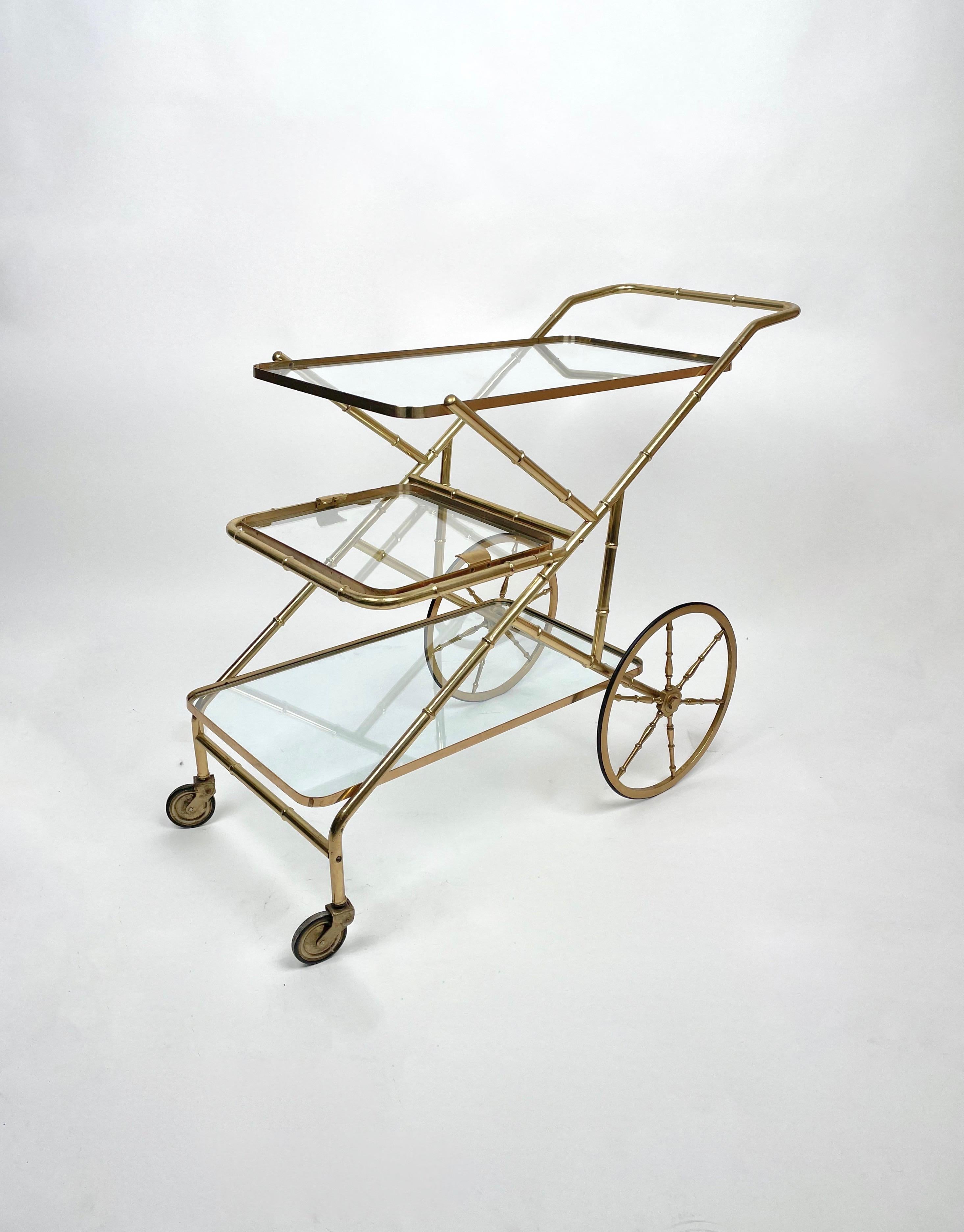 Chariot de service en laiton, structure en faux bambou avec trois étagères en verre, celle du milieu étant amovible, sur roulettes.

Fabriqué en Italie dans les années 1960.
