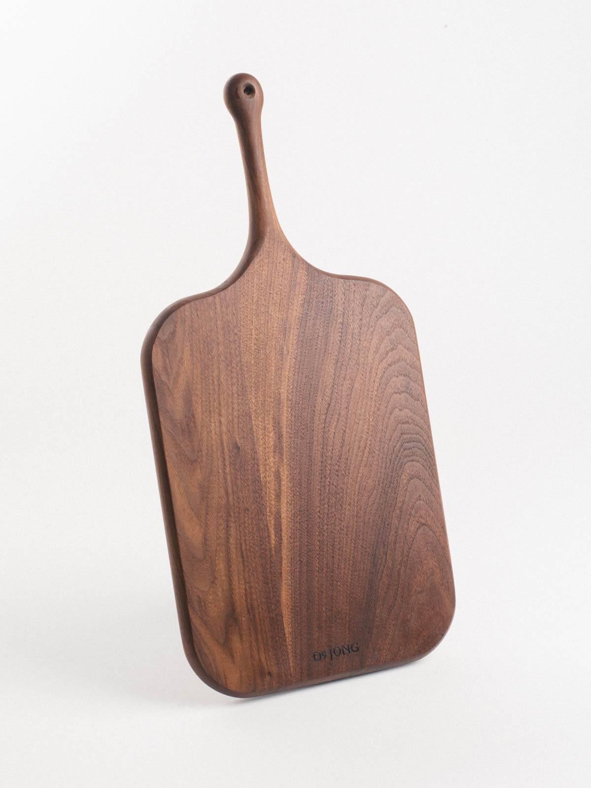 Our serving boards are elegantly shaped with a soft feel. Handles are ideally sized for the palm and include a leather bootlace hanging loop. Half-moon cut-outs serve as a second handle or to direct chopped fare. Each board is shaped, seasoned, and