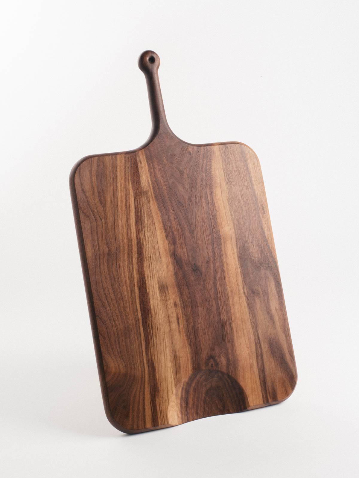 Our serving boards are elegantly shaped with a soft feel. Handles are ideally sized for the palm and include a leather bootlace hanging loop. Half-moon cutouts serve as a second handle or to direct chopped fare. Each board is shaped, seasoned, and