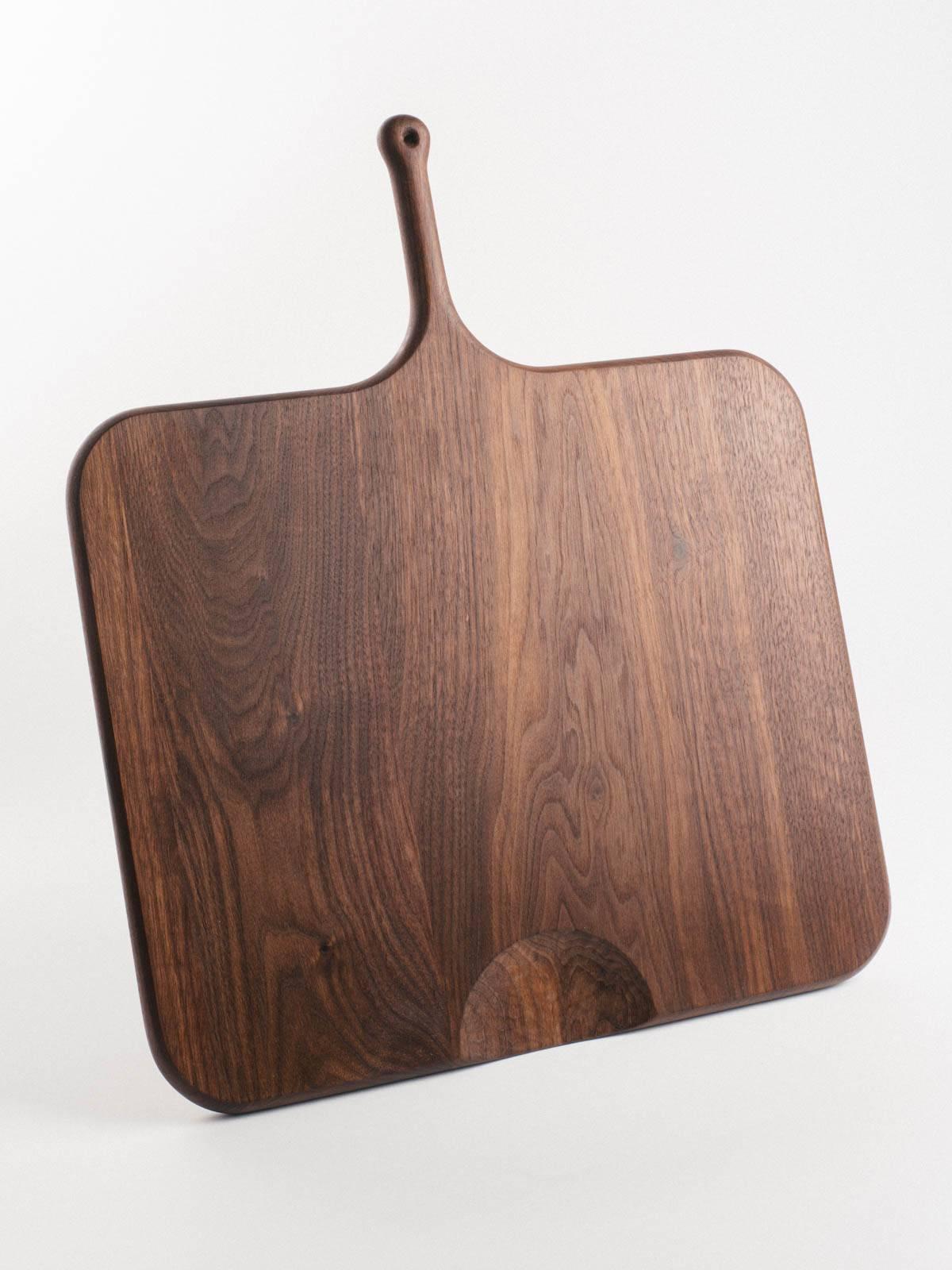 Our serving boards are elegantly shaped with a soft feel. Handles are ideally sized for the palm and include a leather bootlace hanging loop. Half-moon cut-outs serve as a second handle or to direct chopped fare. Each board is shaped, seasoned, and