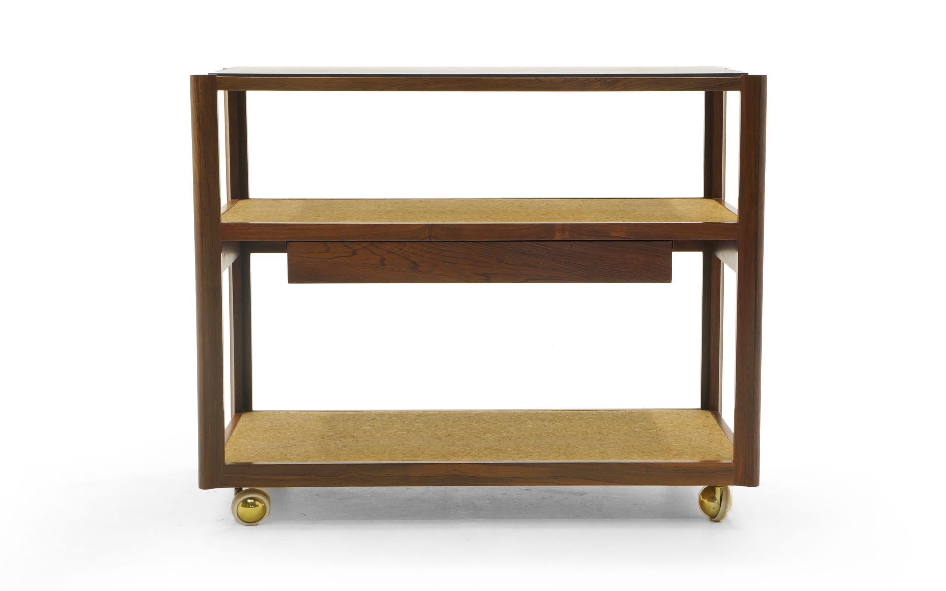 Edward Wormley for Dunbar serving cart or bar trolley with drawer on brass casters. Beautiful mix of materials: Sculpted Brazilian rosewood frame (see details in photos), shelves are cork covered, and the black slate top has been polished to virtual