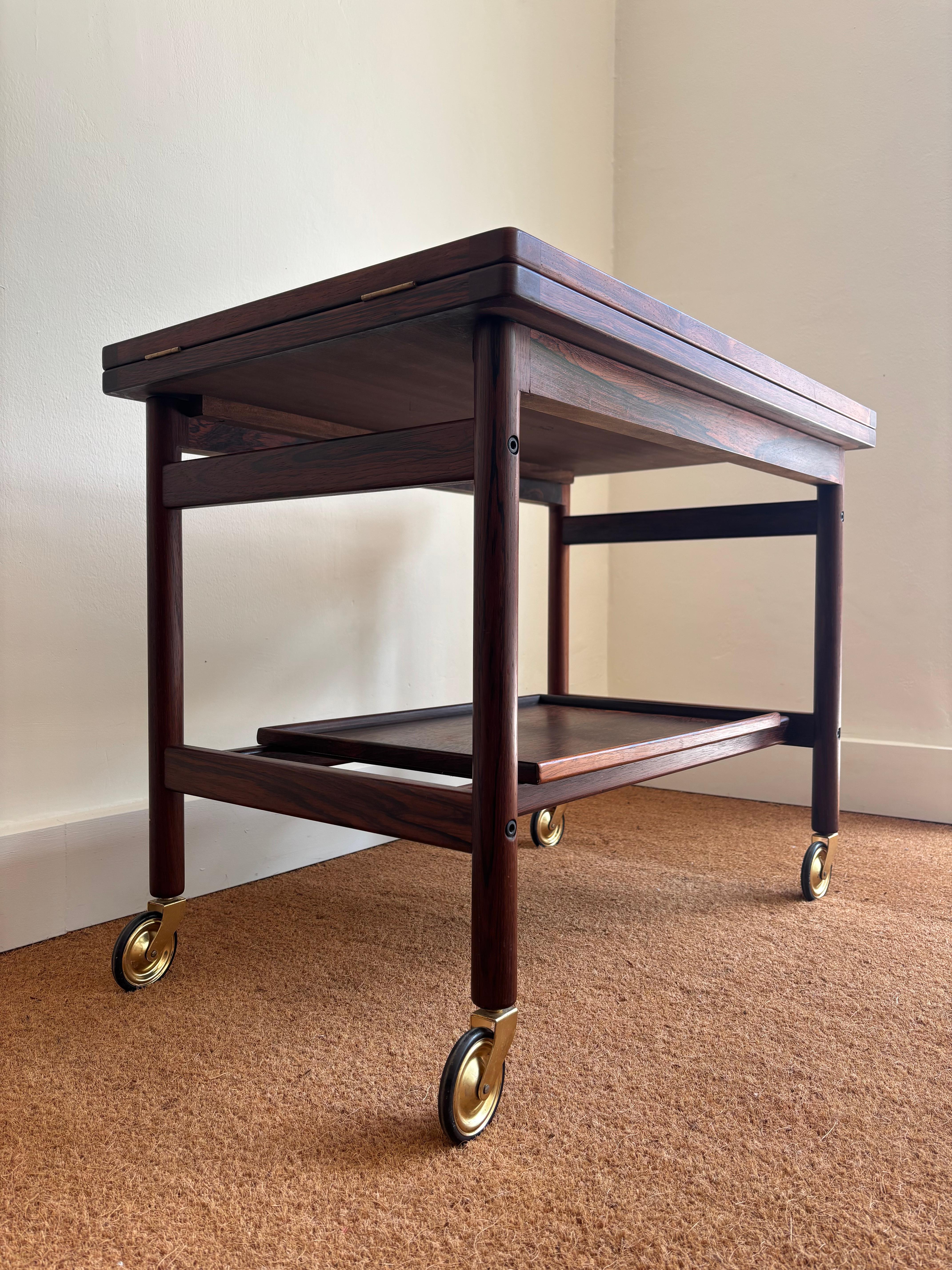 Ein ganz besonderer Servierwagen
Hergestellt von Jason Mobler
Dänemark, 1960er Jahre
Jacaranda-Holz, schwarze Abdeckungen in geöffnetem Zustand, Räder und Scharniere aus Messing

Messungen
48 W cm  x 75 cm L x 60 cm H
Gesamtlänge in geöffnetem