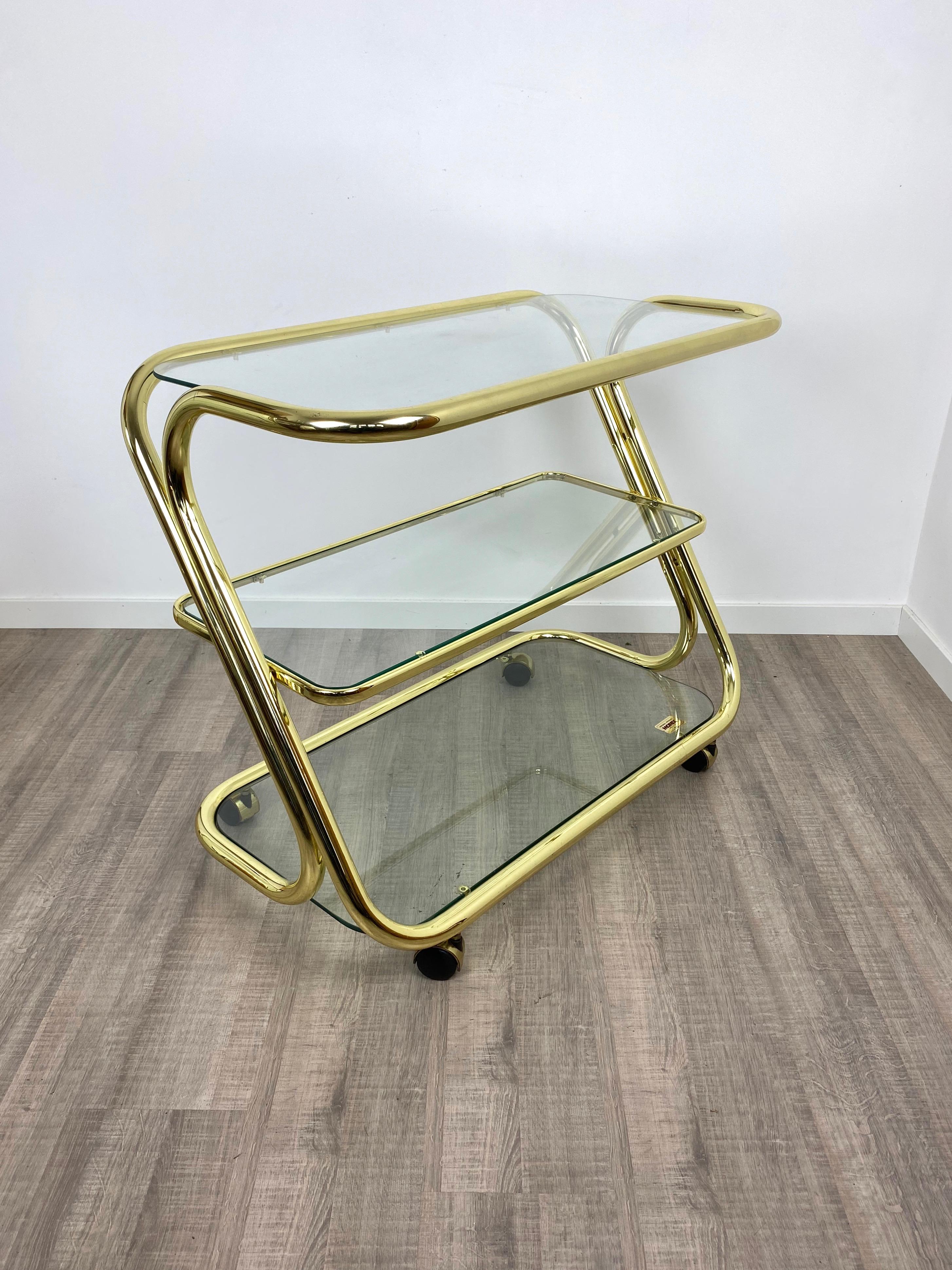 Serving cart trolley in a golden metal structure featuring three glass shelves. 
The item was made in Italy by Morex and has its original label still attached on the lowest shelf.