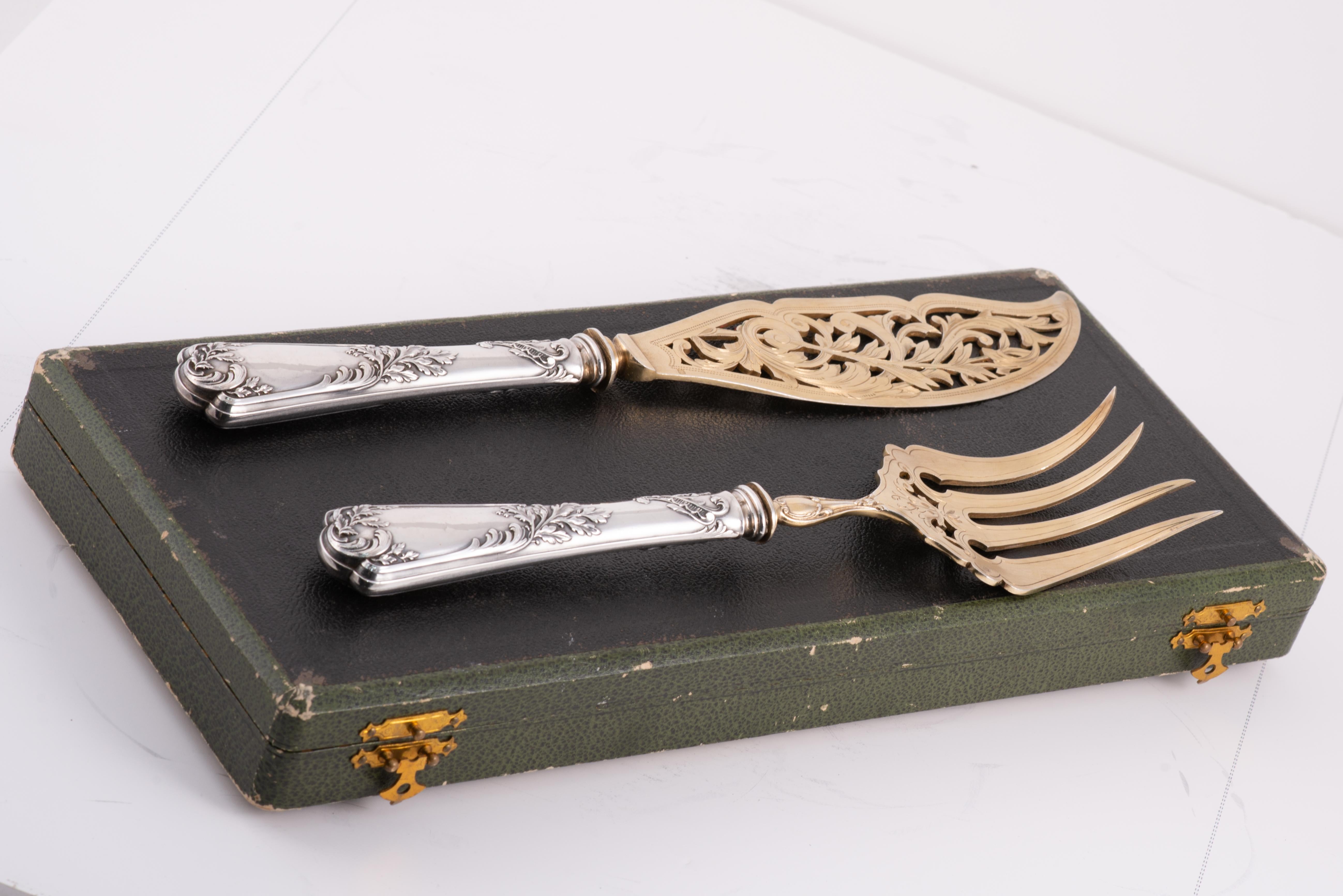 Servierbesteck in einem Etui. Silber, vergoldetes Silber, Textilien, etc. Puiforcat, Frankreich, um 1900. 
Mit Kontrastmarkierungen. 
Ein Paar Servierbesteck mit einem farbigen Silbergriff und einem vergoldeten Griff, verziert mit gravierten und