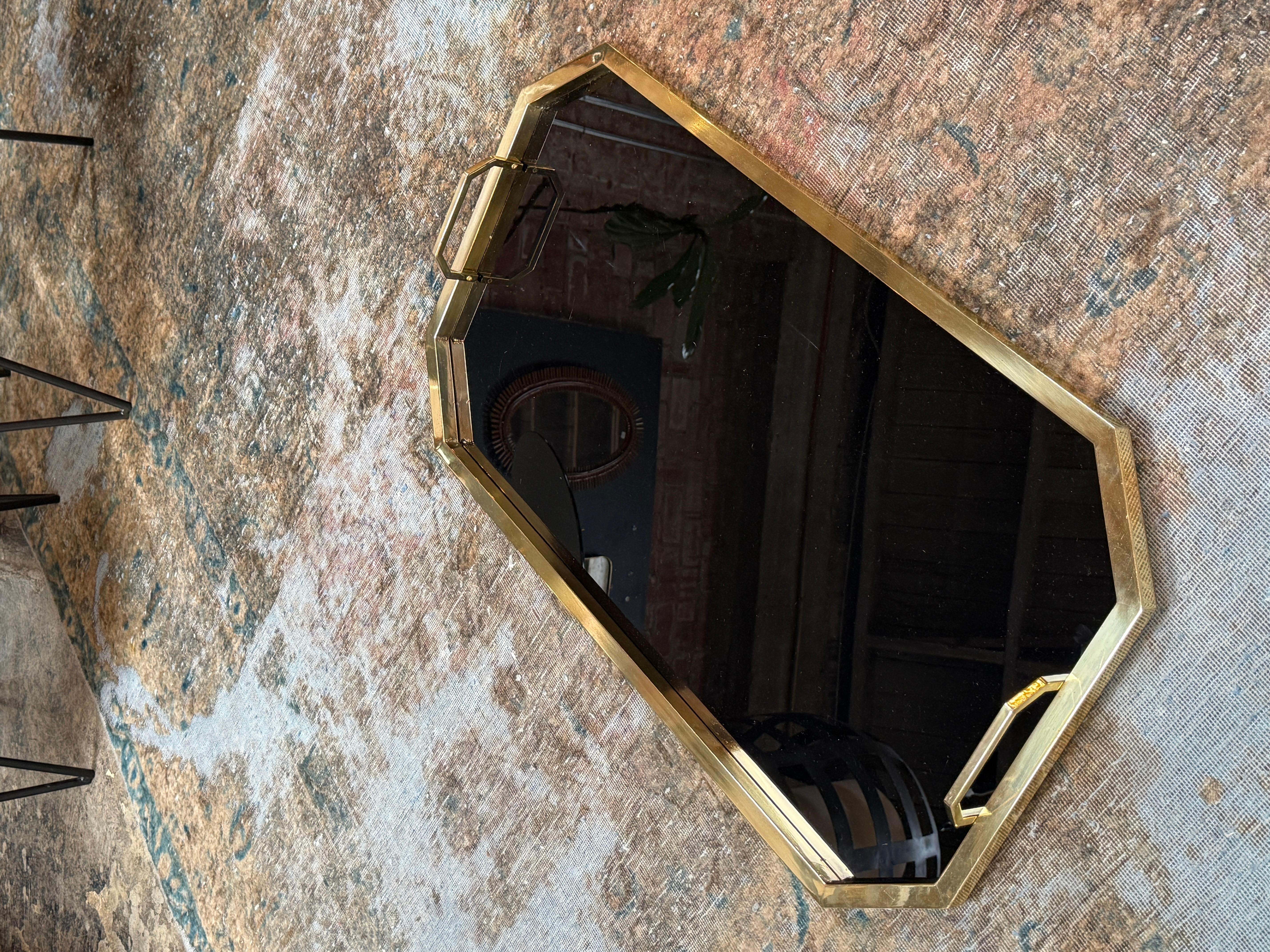 This is an elegant, octagonal serving tray featuring a black reflective surface encased in a gold-toned metal frame. The tray’s angular shape with faceted corners gives it a sophisticated, geometric silhouette. Two matching gold handles are