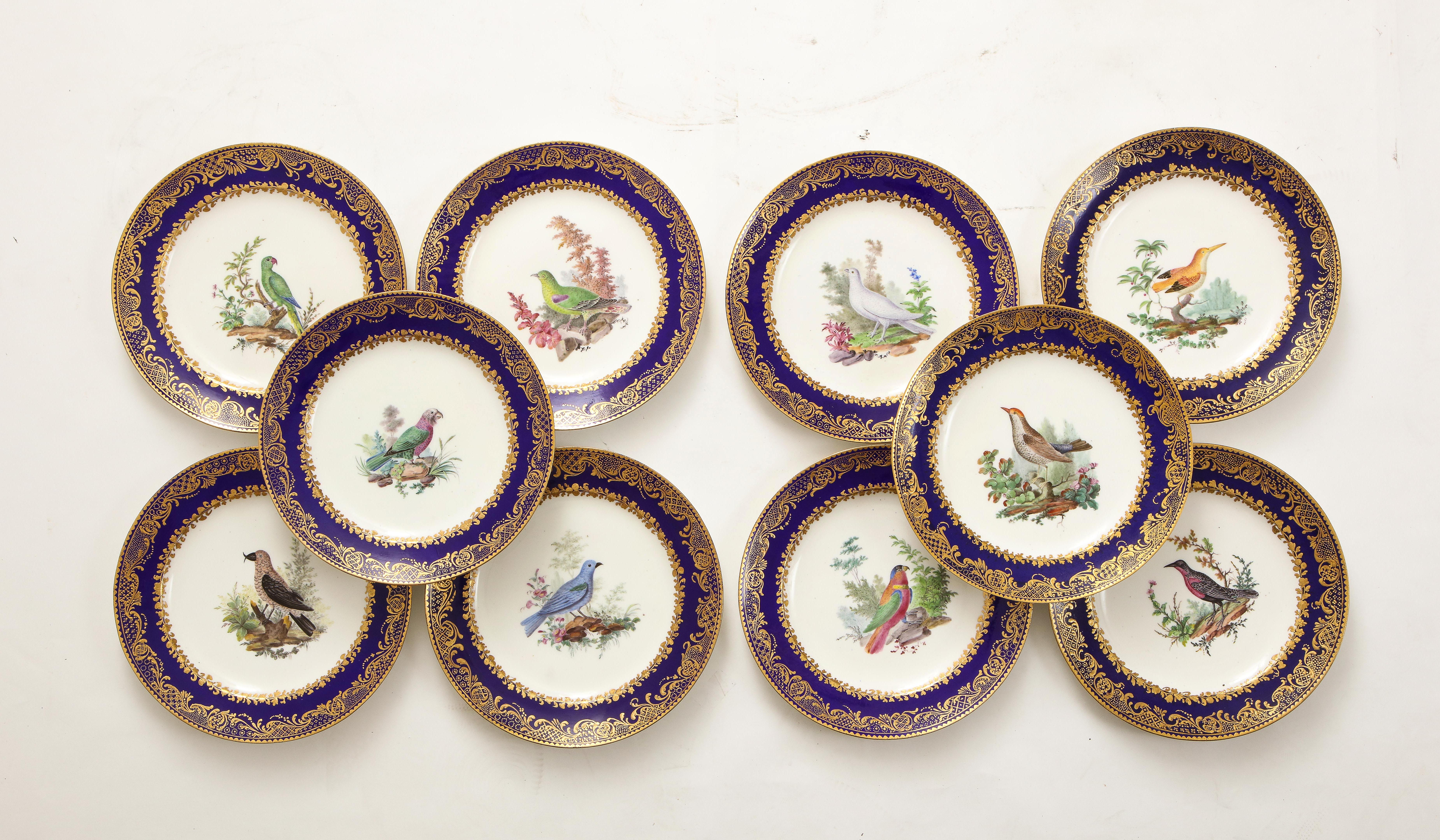 A Magnificent Set of Ten 18th Century French Sevres Dark Blue Ground, Impasto Gilded Decoration, with Variable Center Bird Decorations. The outer rim is decorated in a notched gold band which runs the extent of the border. Just inside the border is