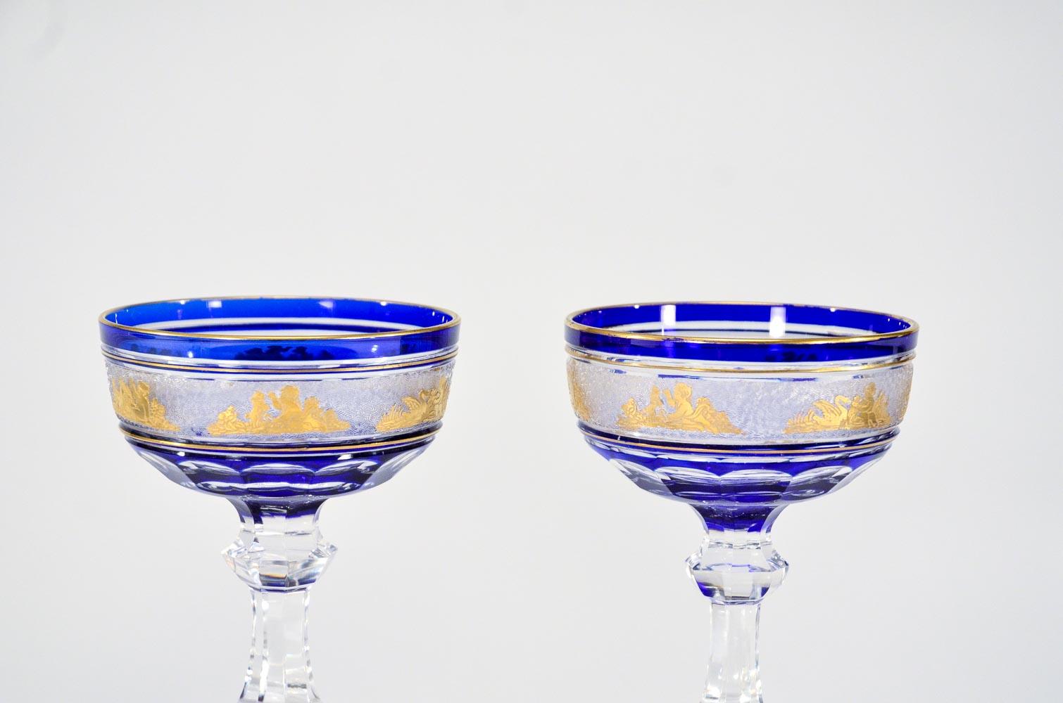 This is a magnificent set of 12 champagne coupes and/or martinis, made by Val Saint Lambert. Each one is hand blown with cobalt crystal overlay, cut to clear with cameo cut frieze of Roman figures embellished with gold leaf. This pattern is one of