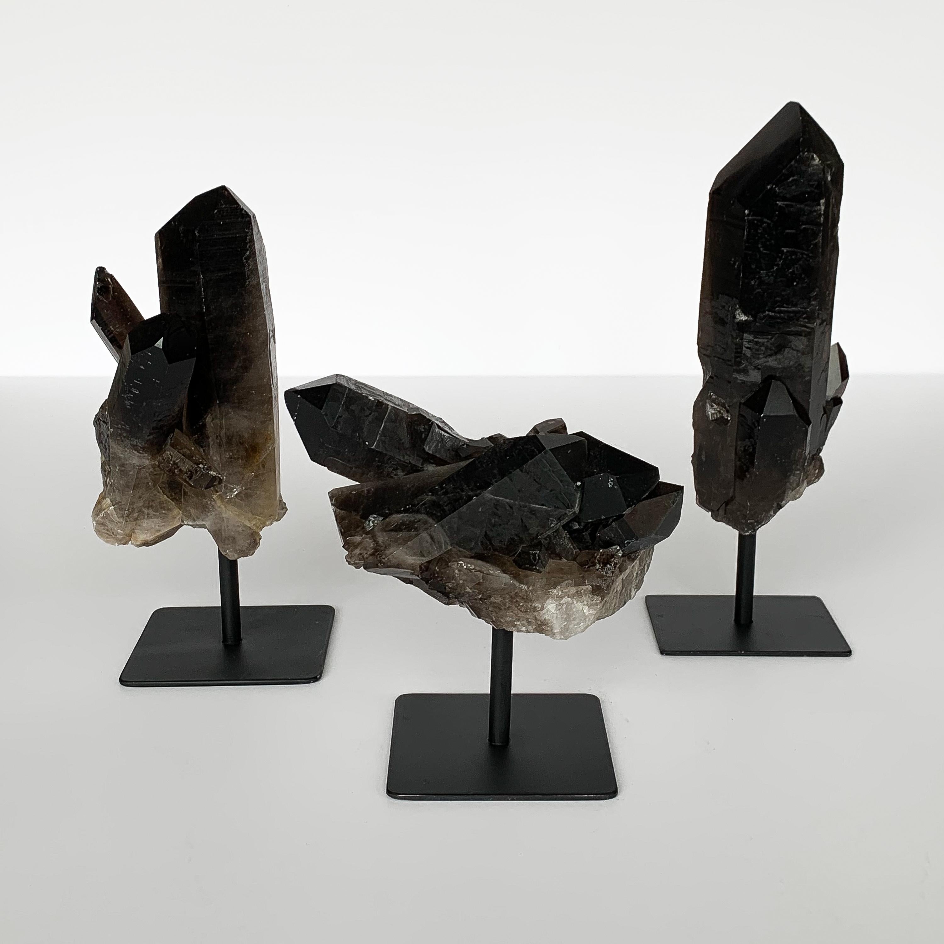 Set of three natural smoky quartz crystal specimens mounted to painted black metal stands.

Measures: Left - 9.75