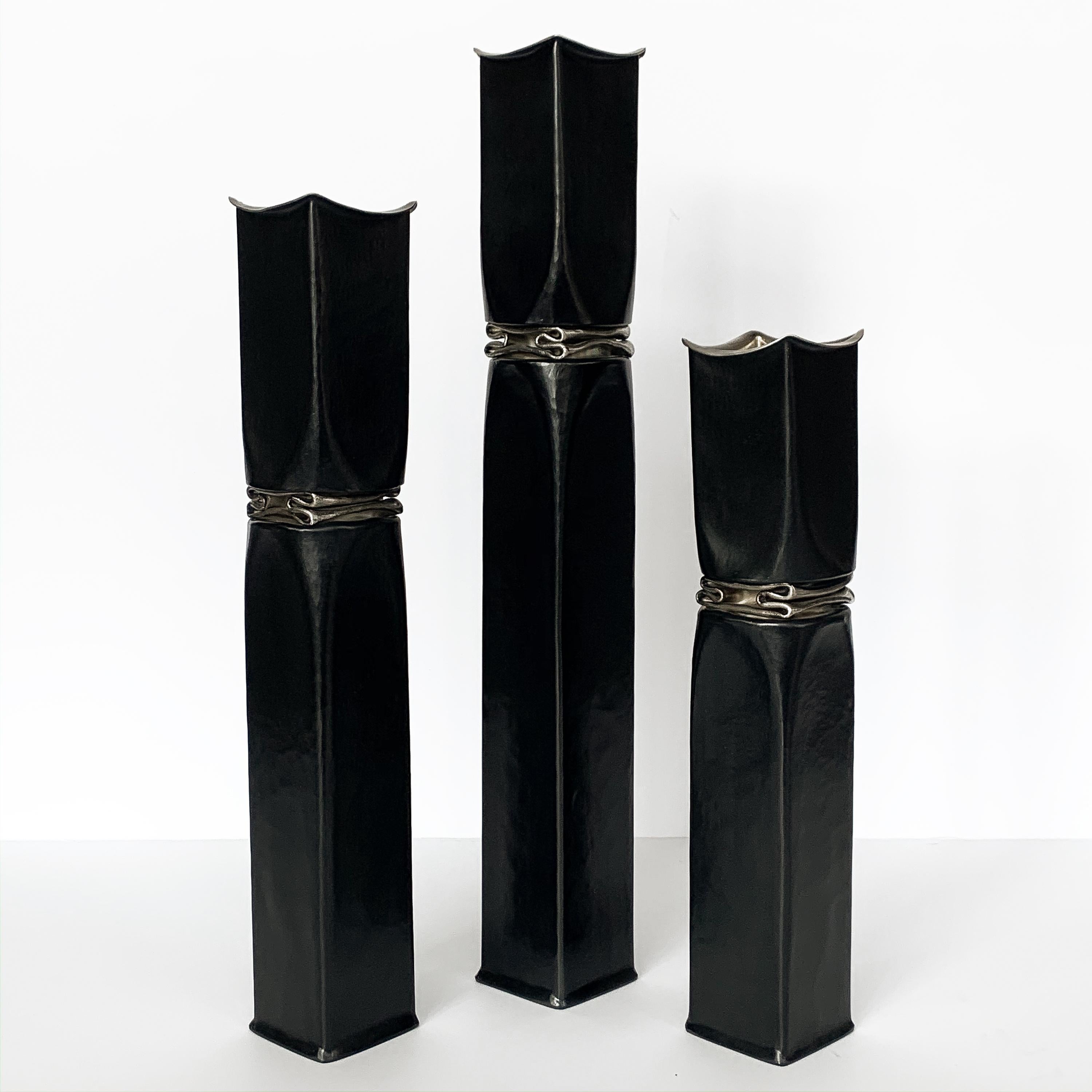 Set of three Thomas Roy Markusen Brutalist black oxidized copper candlesticks. These candle holders or vases feature a black oxidized hammered square copper form with crumbled 