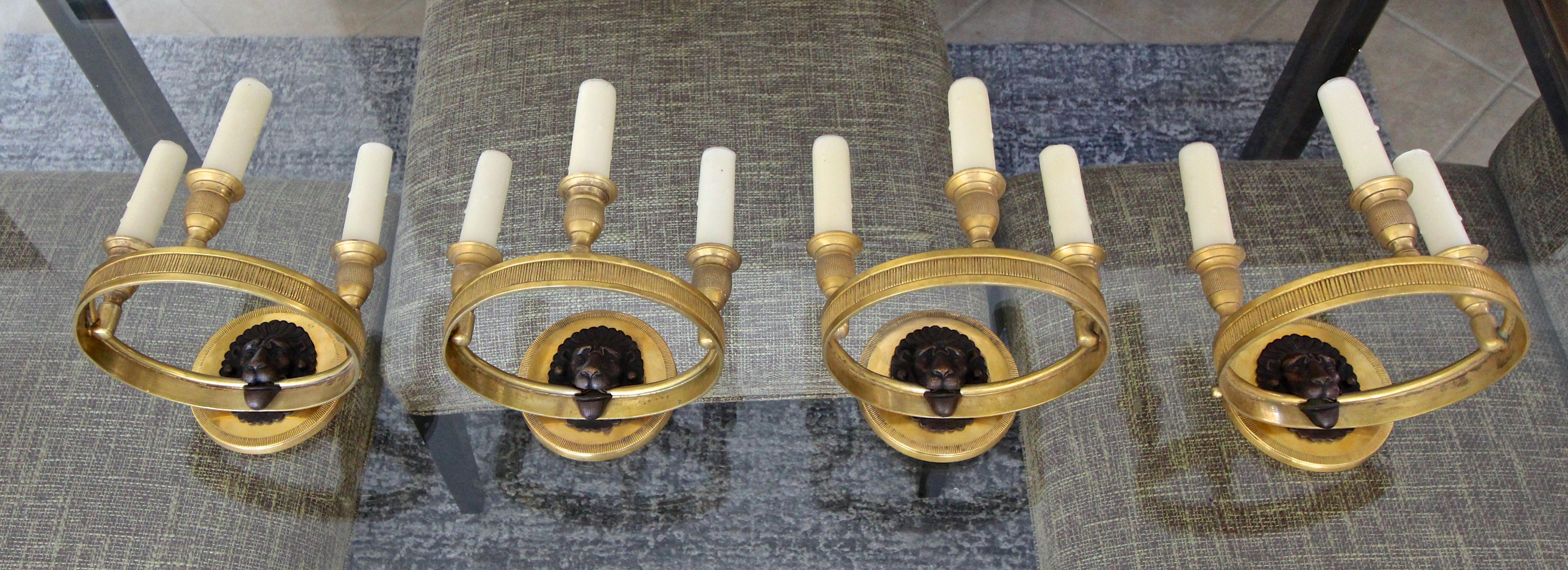 Set of 4 (four) French brass (or bronze) Directoire style wall sconces each with 3 light candleholders. Expert detailing throughout including lion face motif. Each of the 3 lights uses a candelabra size bulb. Back plate 4.5