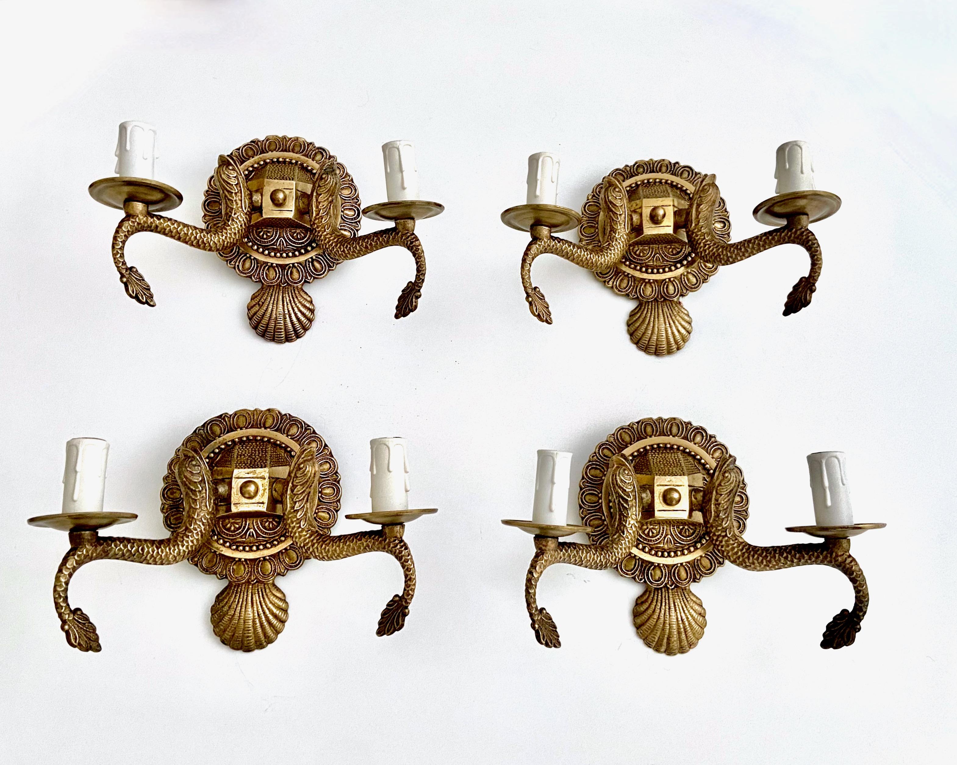 Set of four (4) European two-light neoclassic style brass wall sconces with dolphin and claim shell motif. Expertly crafted with nice quality detailing throughout. Newly wired with new candelabra sockets. Additional pairs available under separate