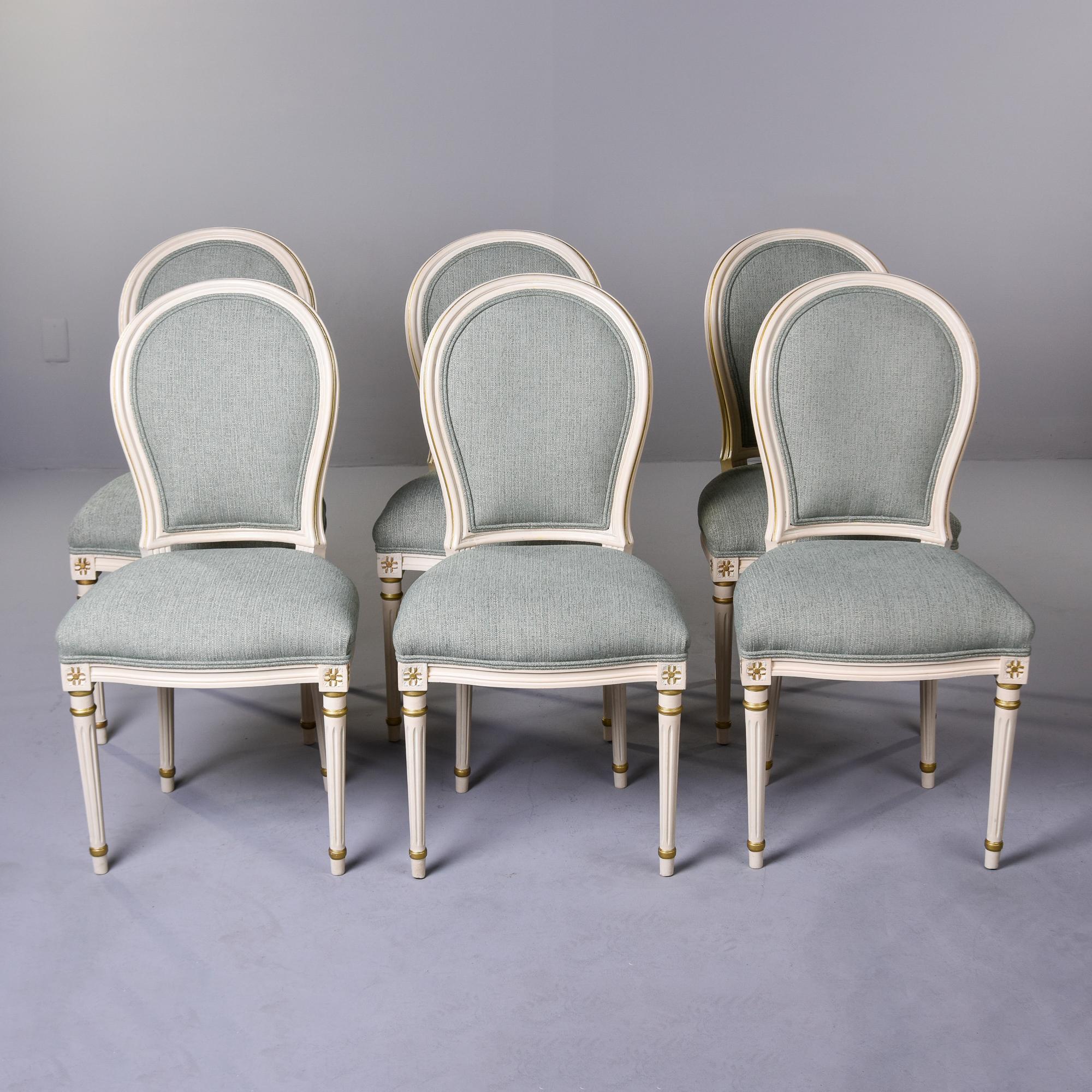 This set of six circa 1920s Louis XVI style dining chairs was found in France. The traditional style frames have rounded backs with carved rosettes at the top of the reeded legs and an off-white painted finish with gilded accents. We had the chairs
