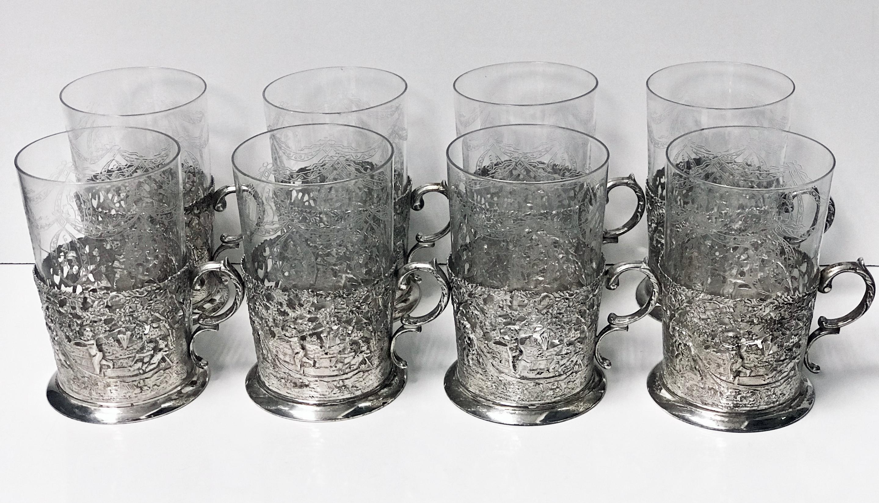 Set of 8 silver glass tea holders, Germany, circa 1900. Each of 0.935 standard silver, depicting beautifully scenes of cherubs, putti and angels amidst foliage. Each glass insert with festoon engraved foliate decoration. Measures: Height 4.50