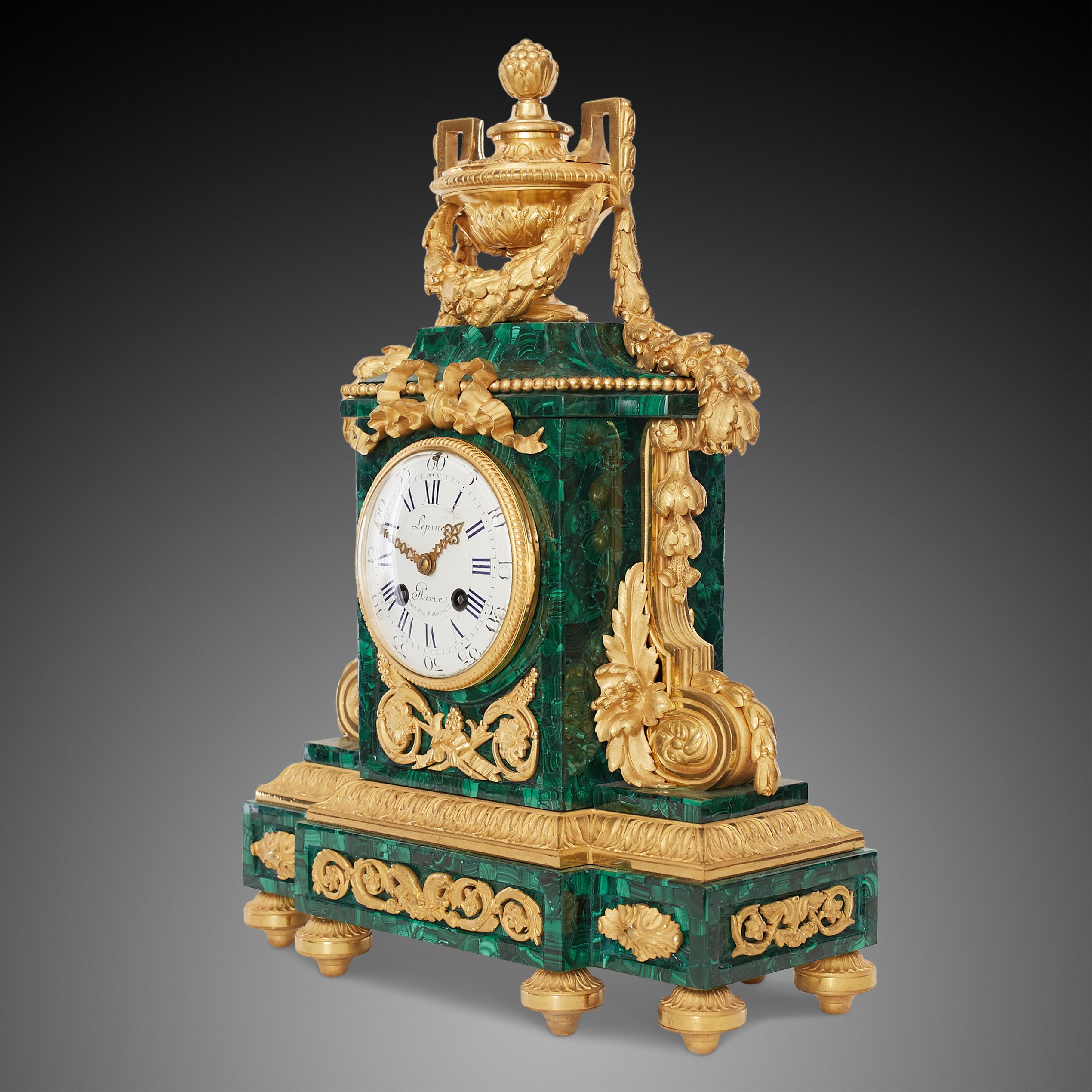 This three-piece clock set consists of a mantel clock and a pair of beautiful malachite candelabra in an ornamental Louis XVI style.

The mantel clock in bronze and malachite in the center has an enamel dial with Roman numerals. The whole is
