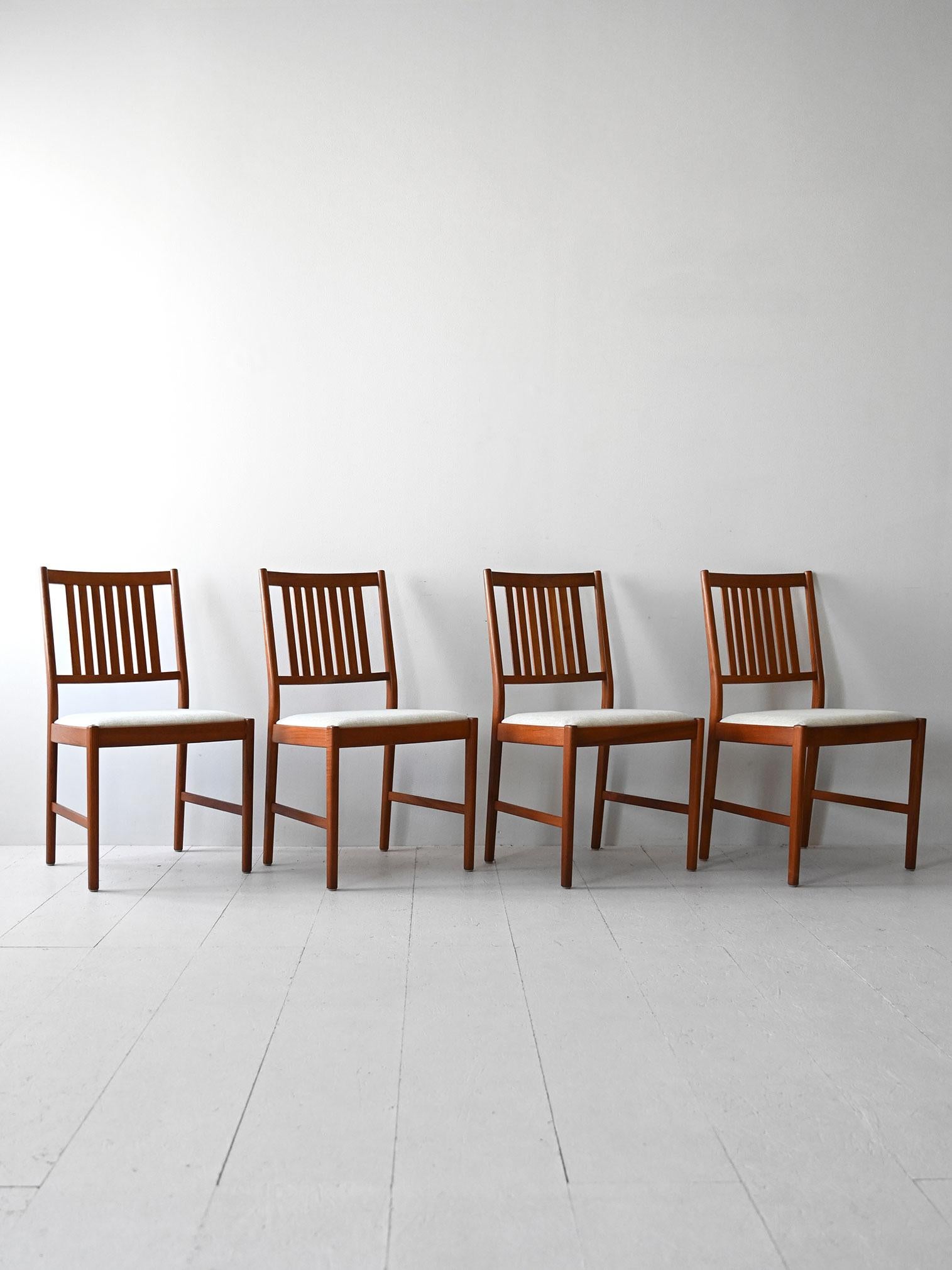 Chaises scandinaves avec structure en teck et assise rembourrée. Ils se distinguent par leur dossier légèrement incliné en lattes de bois. 

L'assise a été retapissée dans un tissu clair. Bon état. Il peut présenter des signes du temps. Veuillez
