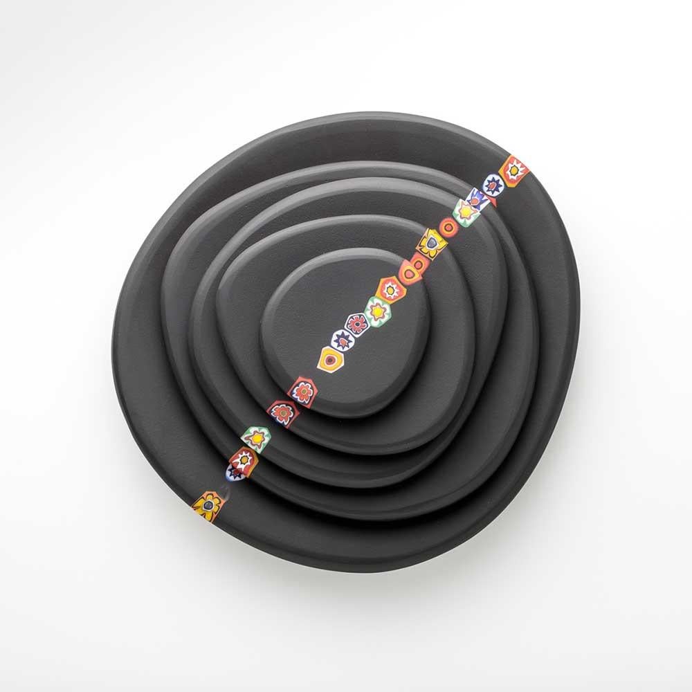 Este elegante juego de 5 platos negros de distintos tamaños, diseñado por la diseñadora Eliana Lorena, evoca los guijarros pulidos por el tiempo. Cada plato está fabricado con la técnica del 