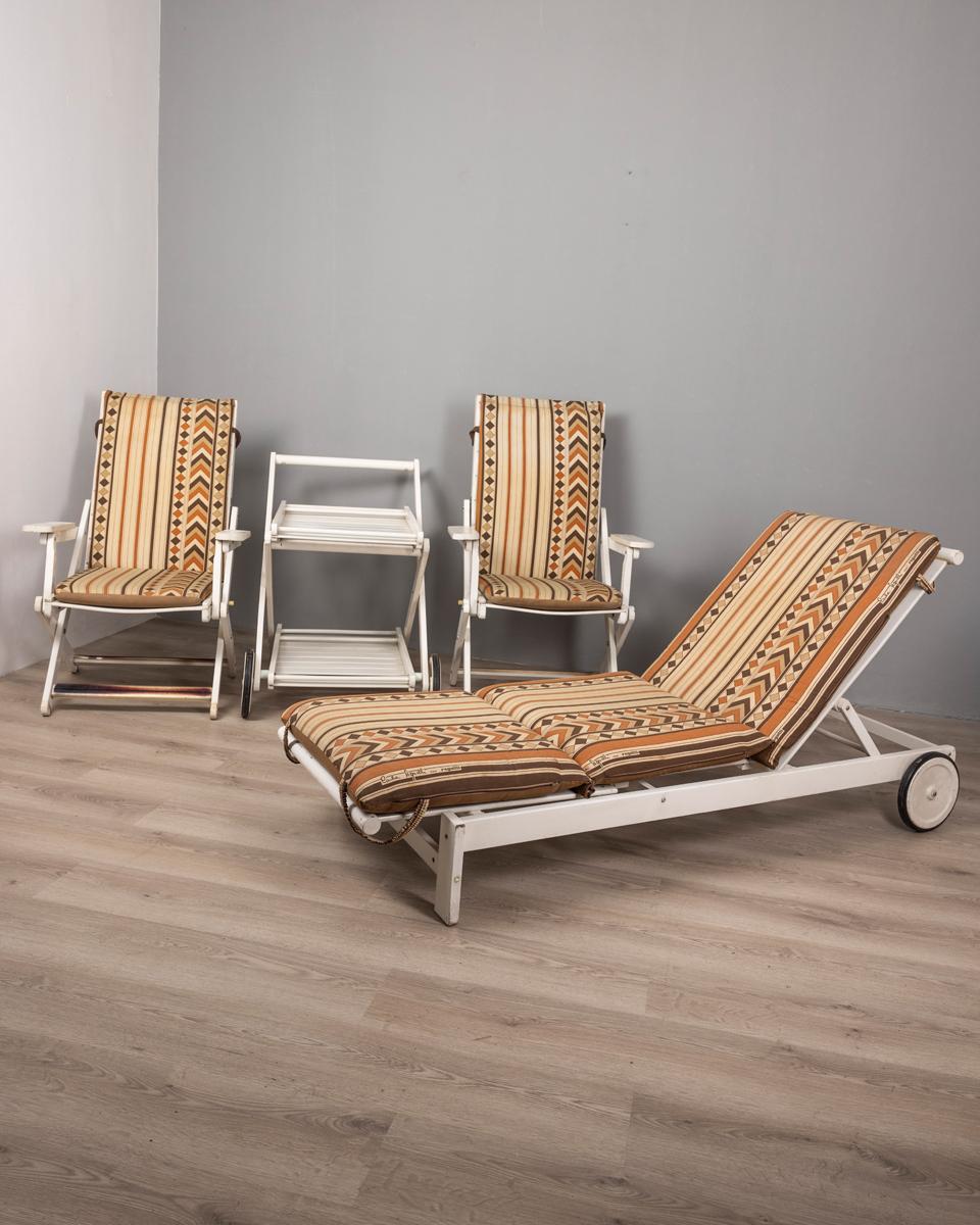 Set of two deck chairs , a deck chair and a trolley, the frames are the white painted wood, the cushions of the deck chairs are upholstered in fabric signed Clara Agnelli for Fratelli Reguitti, 1970s.

CONDITION:
In good, working condition, showing