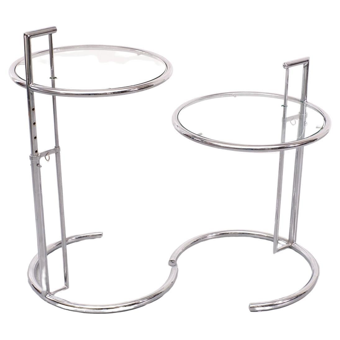 These vintage tubular steel and glass E1027 end tables  was designed by Eileen Gray in 1926. The ingenious design features a chrome-plated tubular steel frame with circular glass tabletop  The table height is adjustable along the base making it a