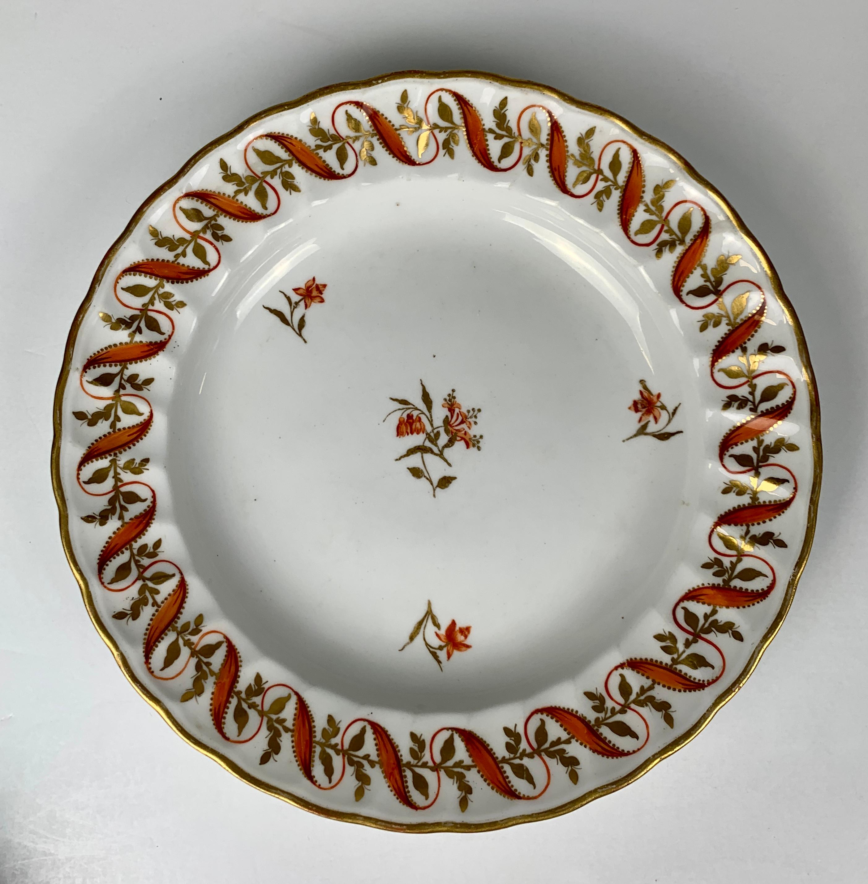 This set of four hand-painted dishes were made by Derby in England late in the 18th century, circa 1790.
The border shows an exquisite wavy orange ribbon that opens and closes while it weaves in and out of a line of golden flowers. 
The center of