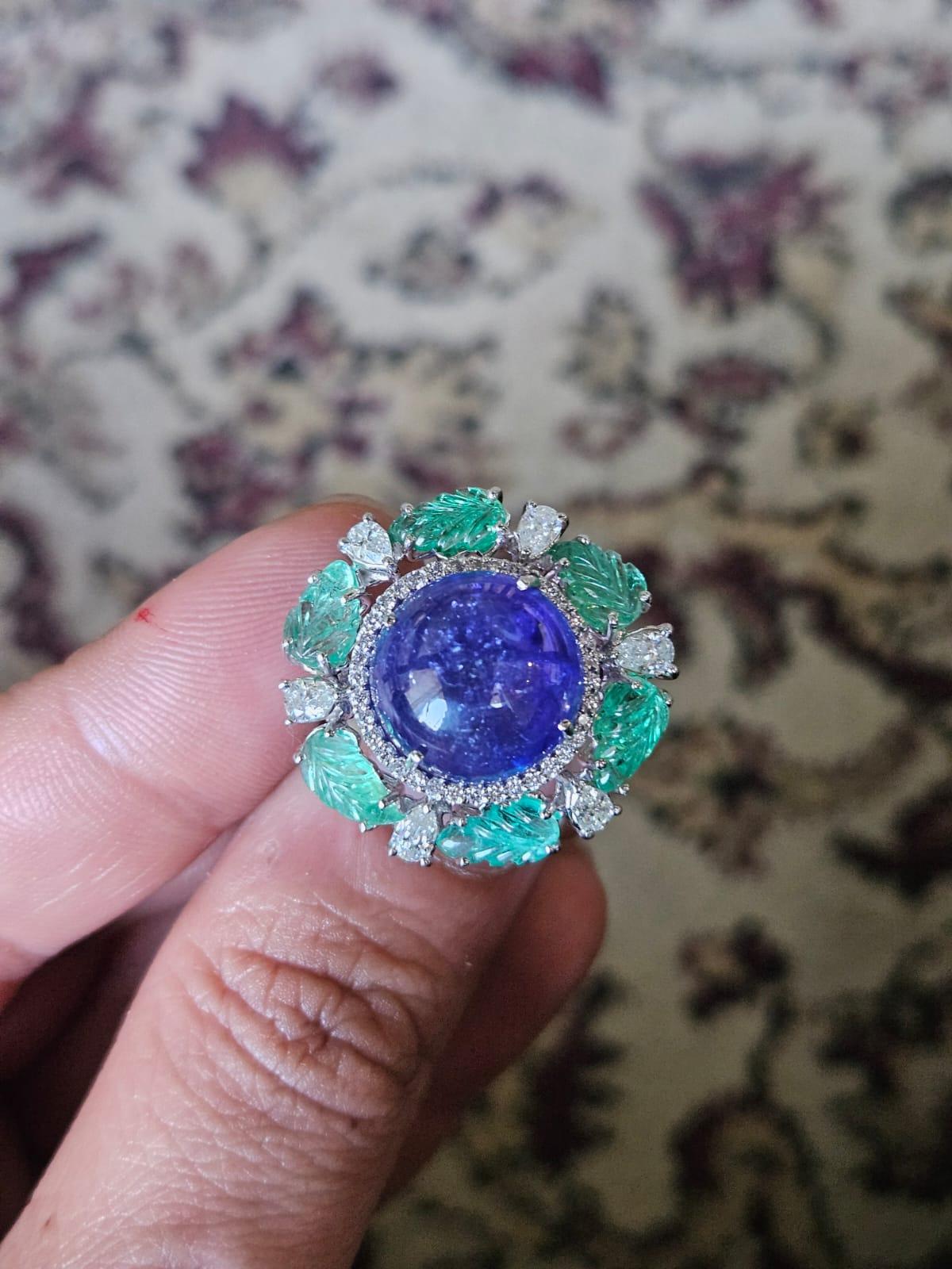 A very gorgeous and beautiful, Tanzanite & Emerald Cocktail Ring set in 18K White Gold & Diamonds. The weight of the Tanzanite Cabochon is 12.59 carats. The Tanzanite is responsibly sourced from Tanzania. The weight of the carved Emeralds is 2.70