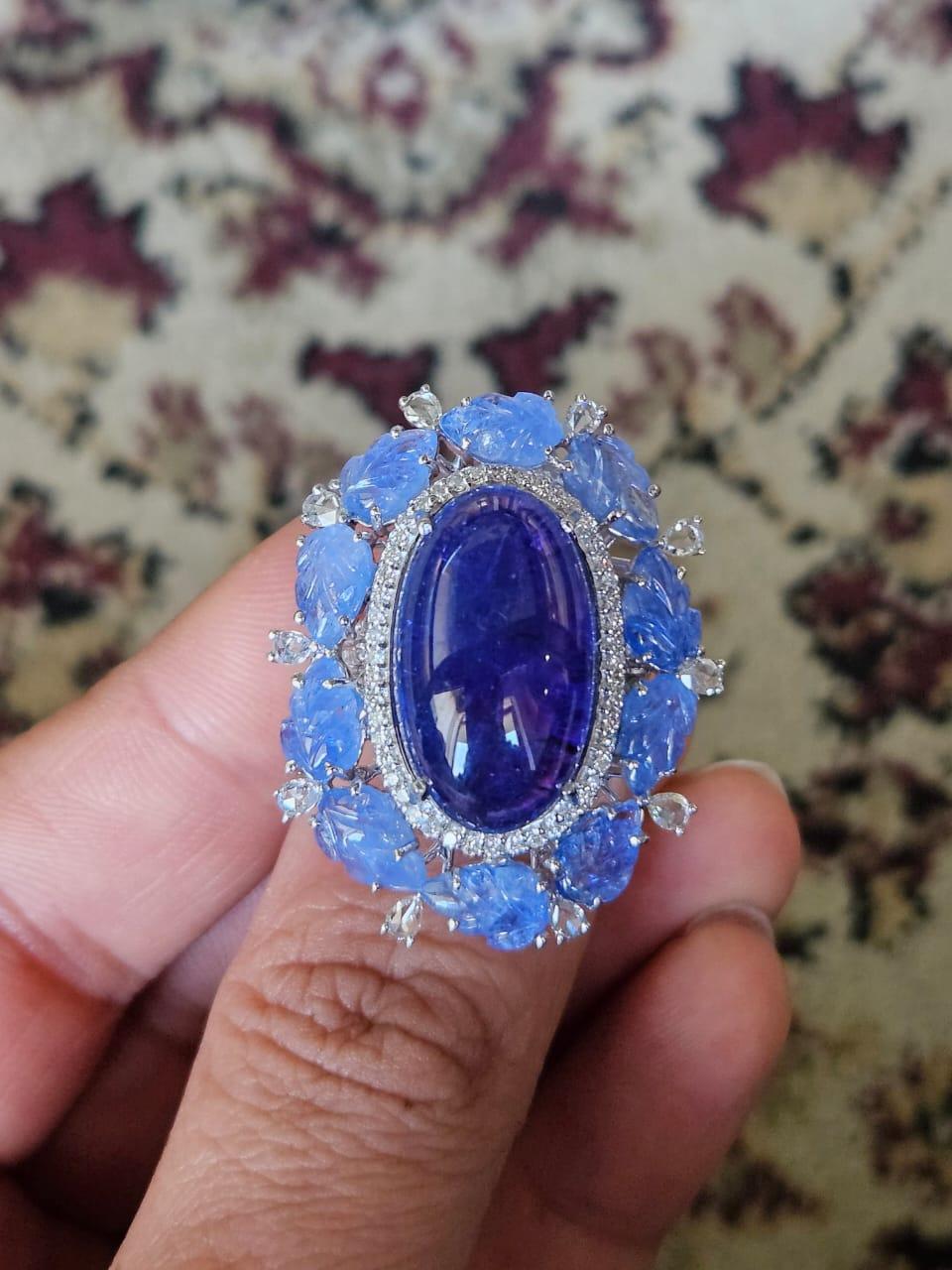 A very beautiful and gorgeous, Tanzanite & Blue Sapphire Cocktail Ring set in 18K White Gold & Diamonds. The weight of the Tanzanite Cabochon is 20.95 carats. The Tanzanite is responsibly sourced from Tanzania. The weight of the carved Blue