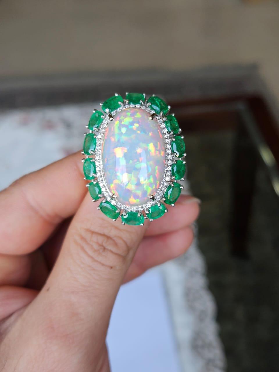 A very gorgeous and beautiful, modern style, Ethiopian Opal & Emeralds Cocktail Ring set in 18K White Gold & natural Diamonds. The weight of the Opal Cabochon is 21.06 carats. The Opal has a green - orange play of colour and is of Ethiopian origin.