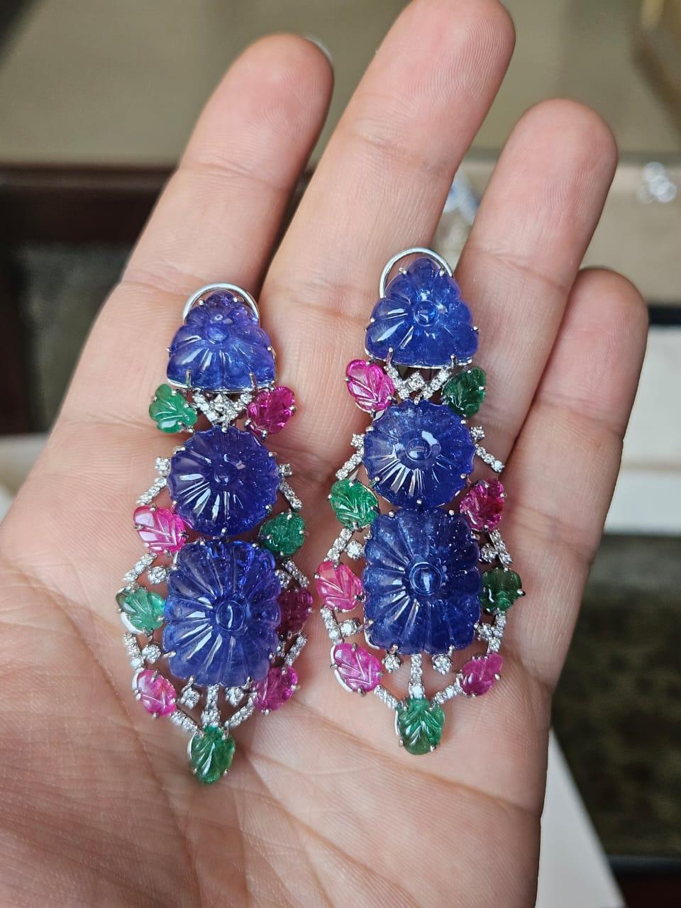 Magnifiques boucles d'oreilles chandelier en or blanc 18 carats et diamants naturels, composées de tanzanite, d'émeraude et de rubis, de style moderne. Le poids des tanzanites sculptées est de 101.30 carats. Les tanzanites proviennent de Tanzanie.