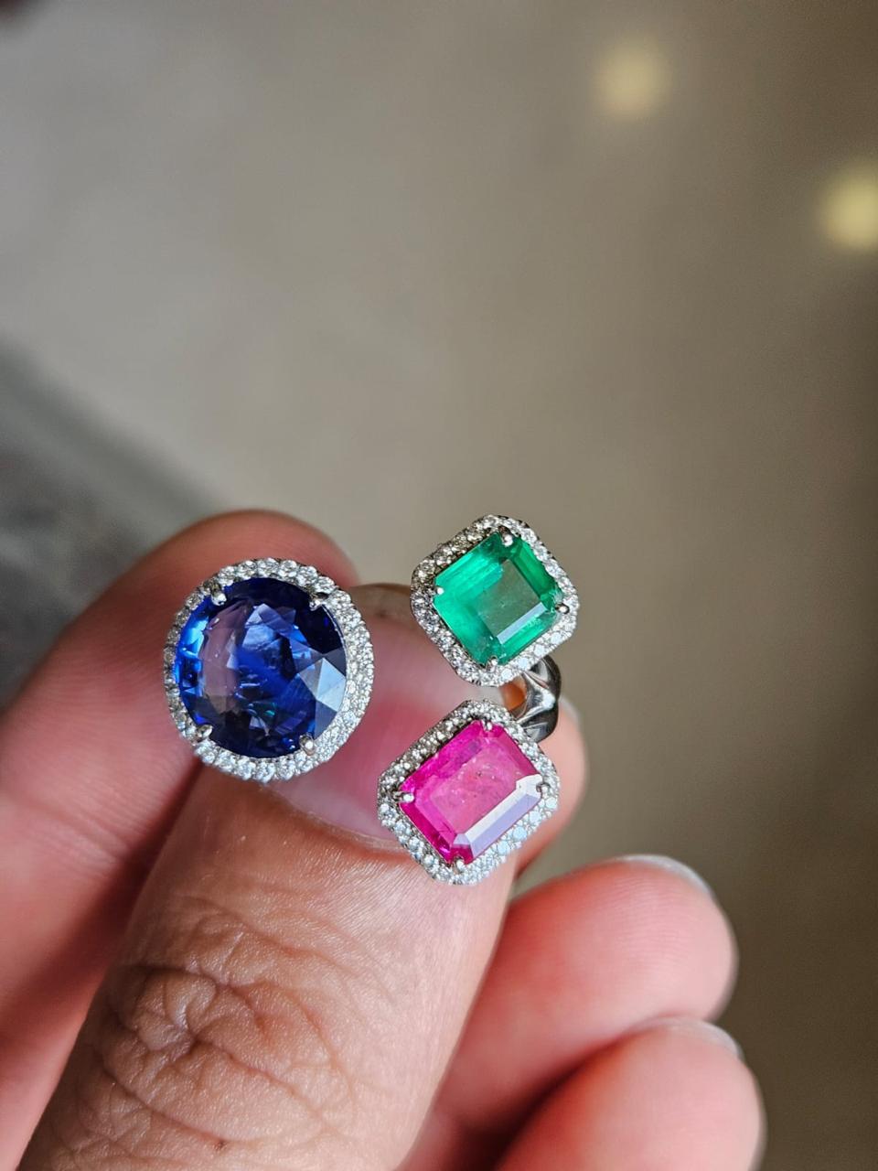 A very gorgeous and beautiful, one of a kind, Emerald, Ruby & Blue Sapphire Three Stone/ Cocktail Ring set in 18K White Gold & Diamonds. The weight of the round Blue Sapphire is 3.71 carats. The Blue Sapphire is of Ceylon (Sri Lanka) origin. The