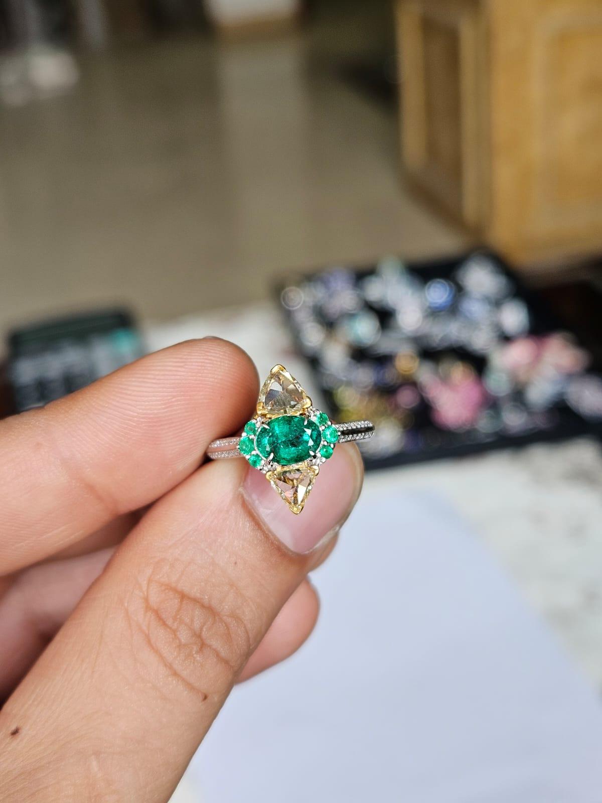 Un precioso anillo de compromiso de esmeralda de estilo moderno, engastado en oro blanco de 18 quilates y diamantes naturales. El peso combinado de las Esmeraldas es de 1.03 quilates. Las Esmeraldas son completamente naturales, sin ningún