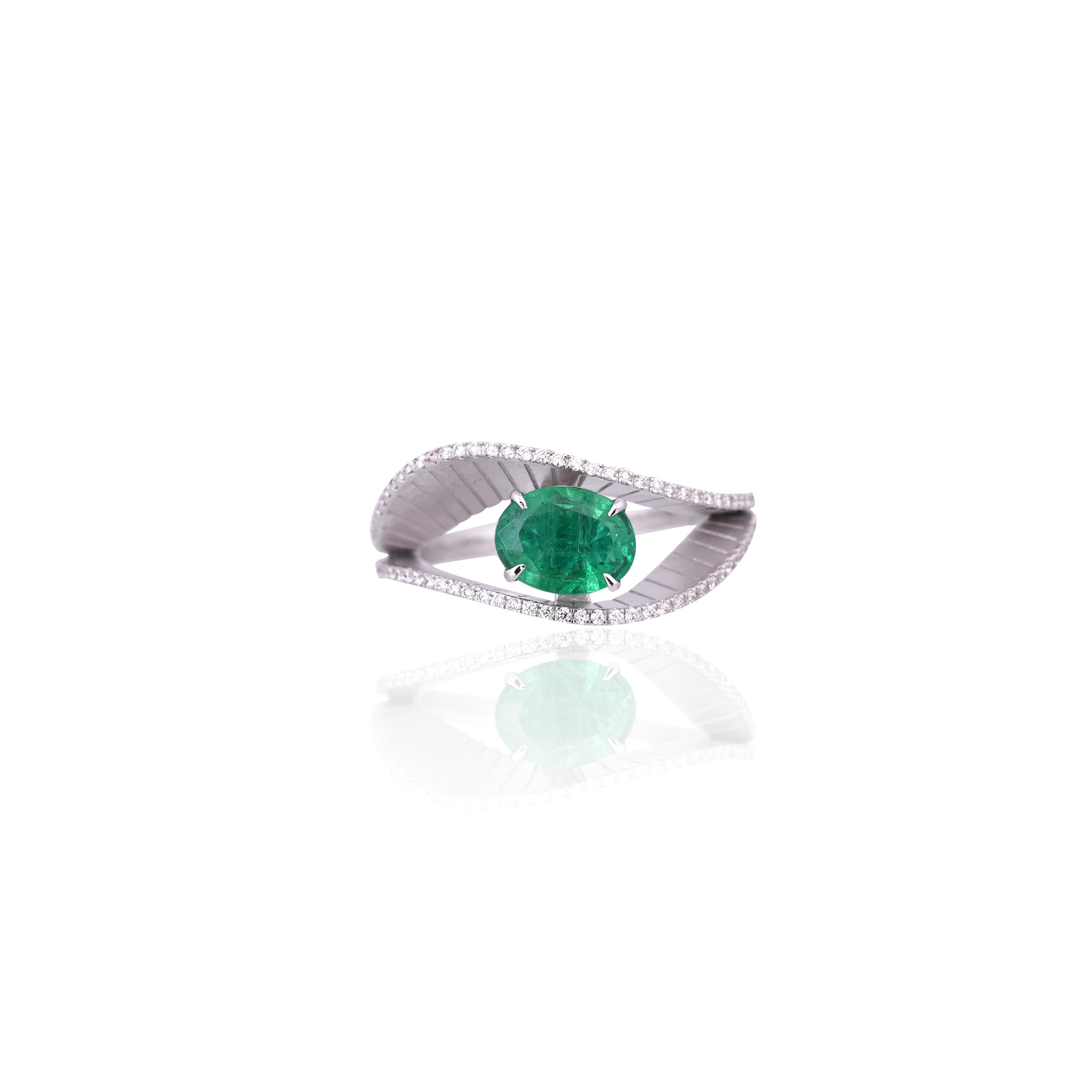 Un precioso anillo de compromiso de esmeralda de estilo moderno, engastado en oro blanco de 18 quilates y diamantes naturales. El peso de la Esmeralda ovalada es de 0.92 quilates. La Esmeralda es completamente natural, sin ningún tratamiento y es de