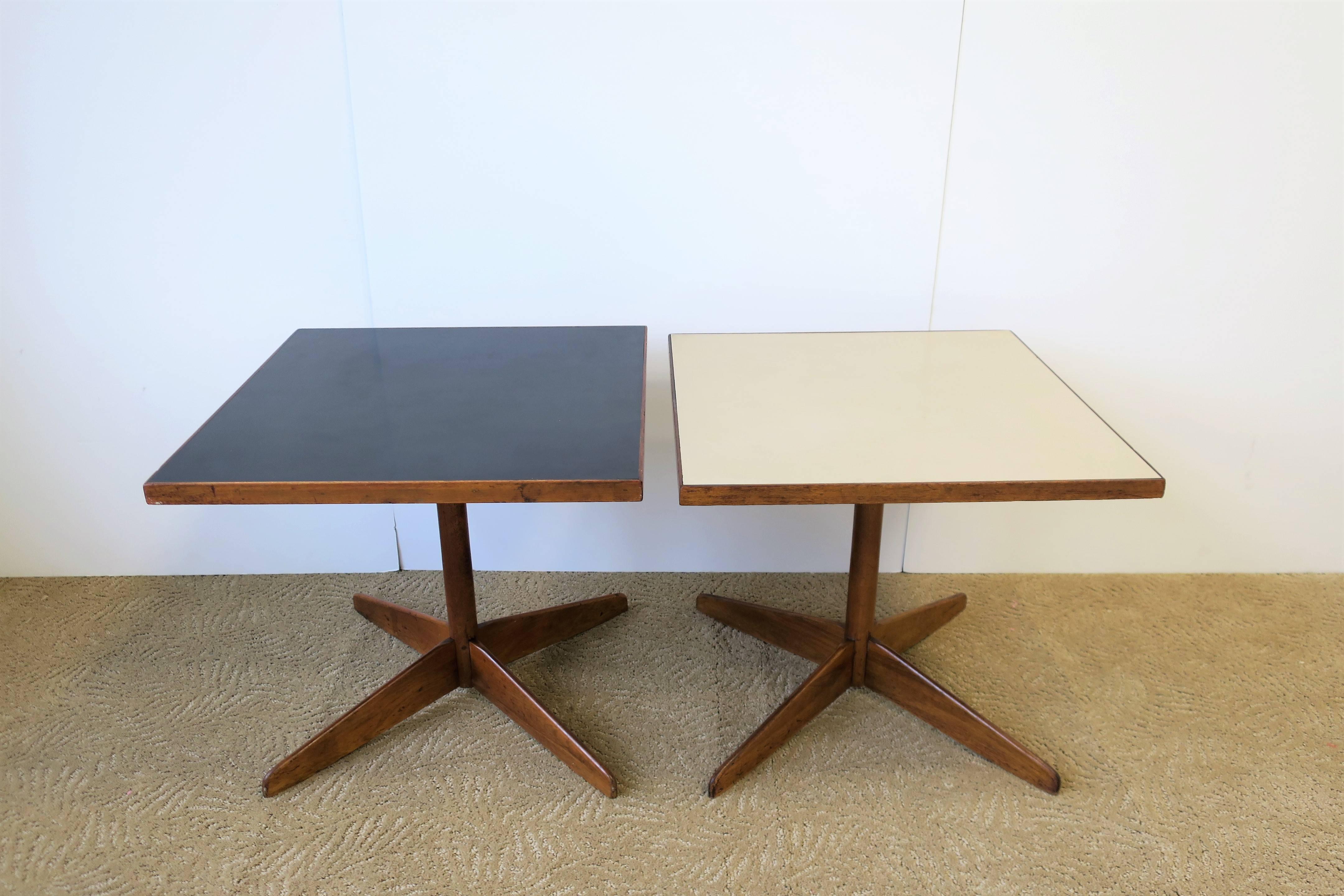 A set/pair of Mid-Century Modern period square side, drinks, or end tables, circa 1960s. Table are lightweight in nature, and both have veneered tops; black and beige/cream, with wood base/frame. Tables are a convenient size with each measuring