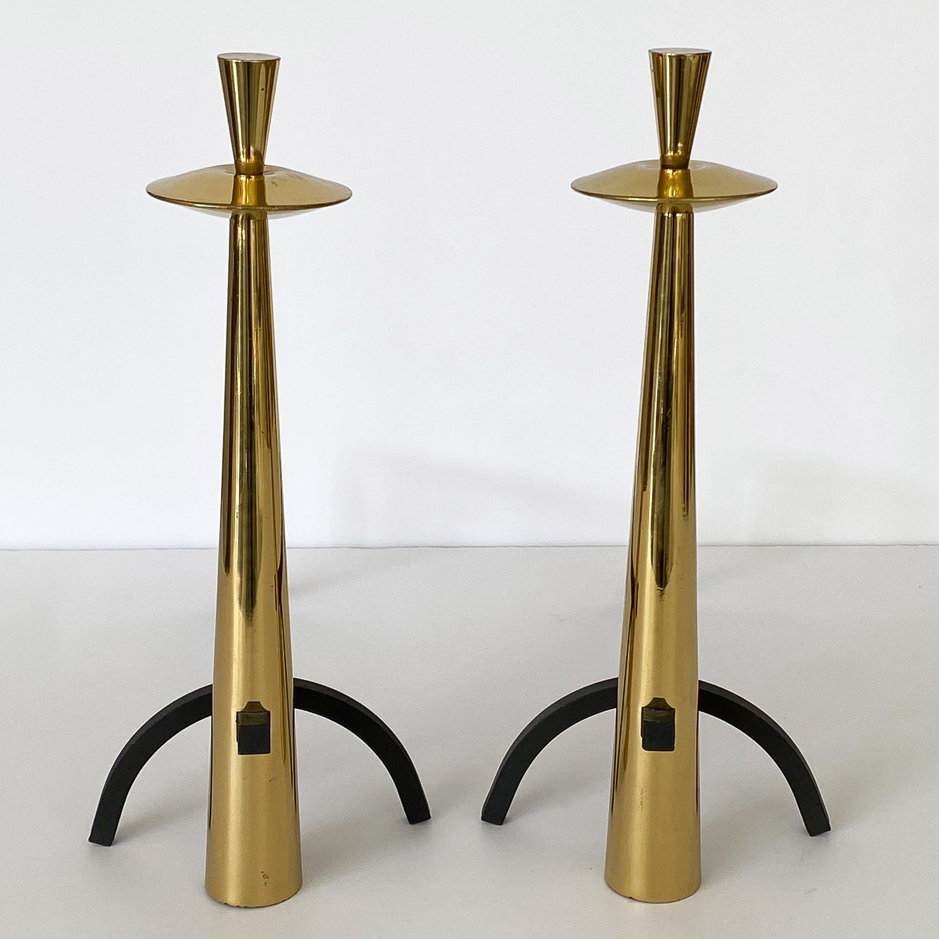 Set / pair modernist brass fireplace andirons, circa 1960s. Striking pair of modern brass andirons with blackened wrought iron. These andirons feature an elongated conical form with stylized saucer shape detail and conical finials. Blackened iron
