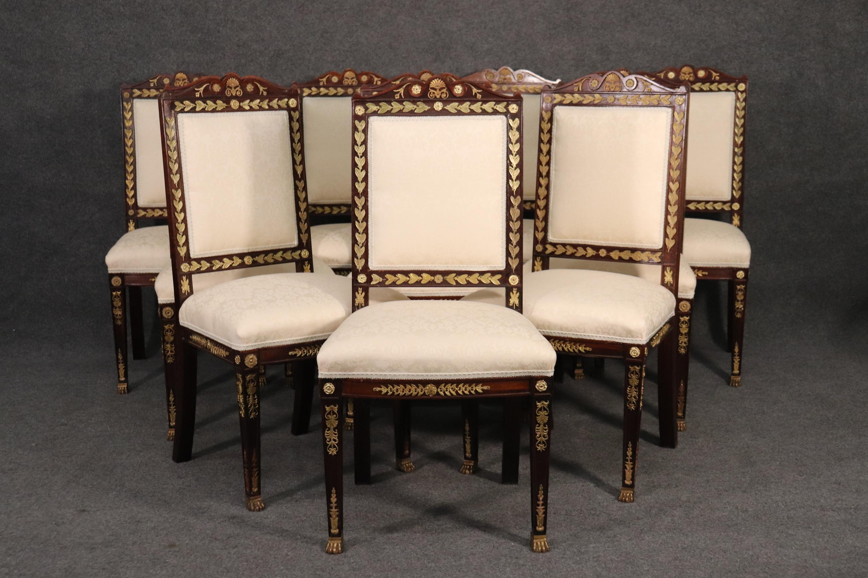 This is a beautiful set of 10 bronze mounted walnut French Empire dining chairs. The chairs have bright bronze in gold and a beautiful contrasting dark walnut frame. The frames are adorned with bronze ormolu and feet. The chairs each measure 40 tall