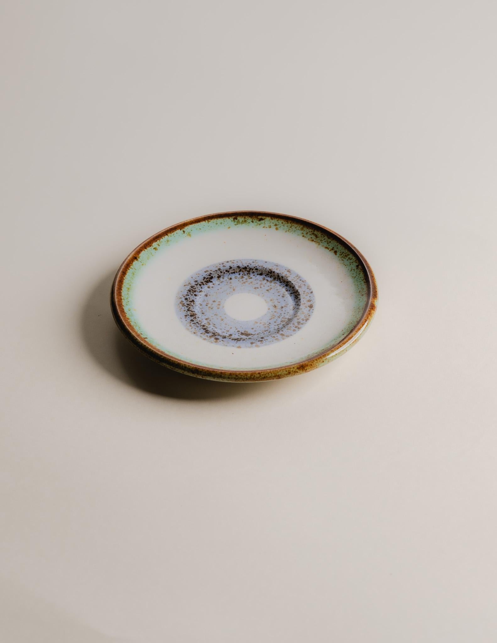 Ensemble de 10 assiettes à café en céramique émaillée, La Roue, Vallauris, années 1960.
Chacune est signée au verso et présente un motif circulaire dans des tons bleus, verts et bruns, reflétant le style moderniste de la production de La Roue. La